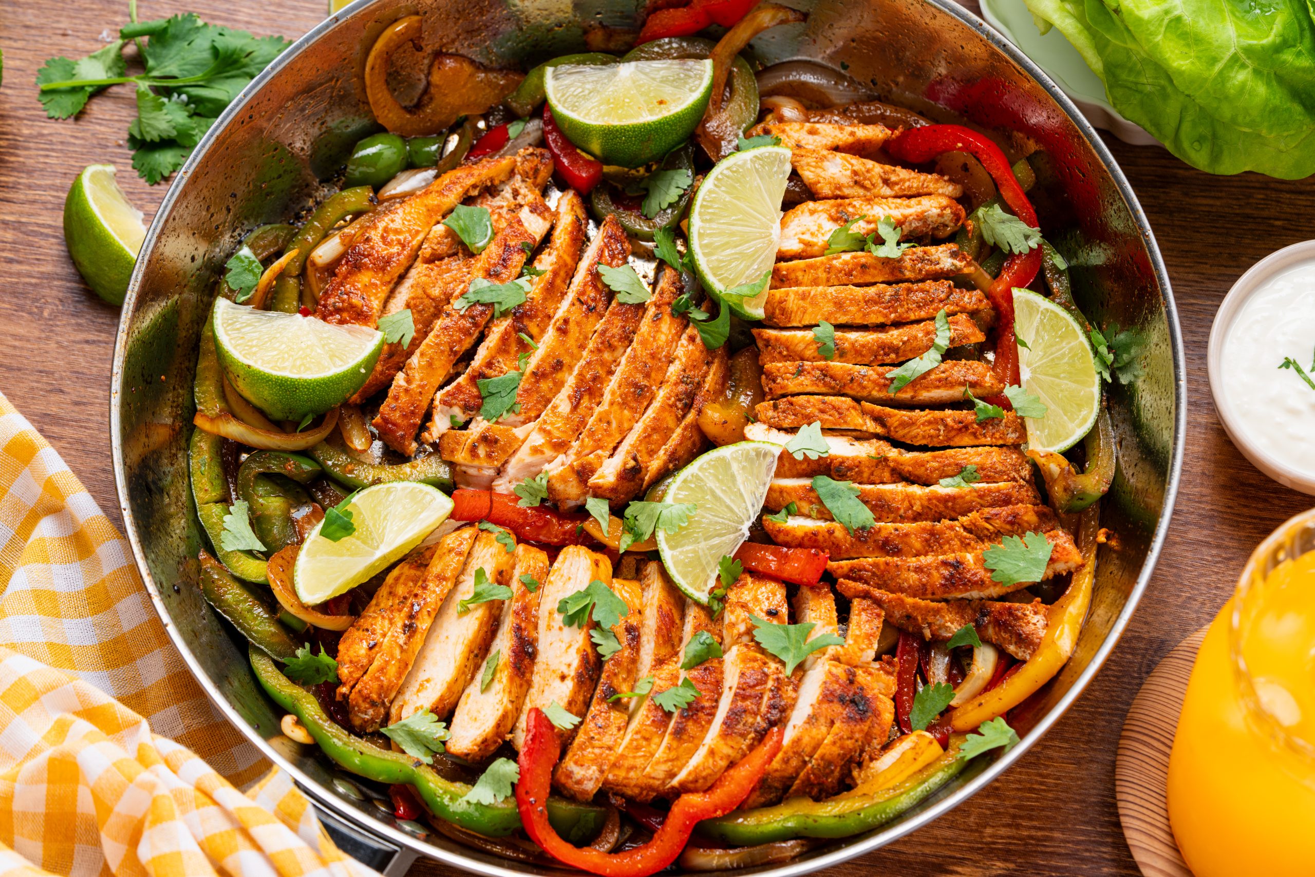 A vibrant skillet of chicken fajitas featuring sliced chicken, sautéed bell peppers, onions, cilantro, and lime wedges, photographed from above.