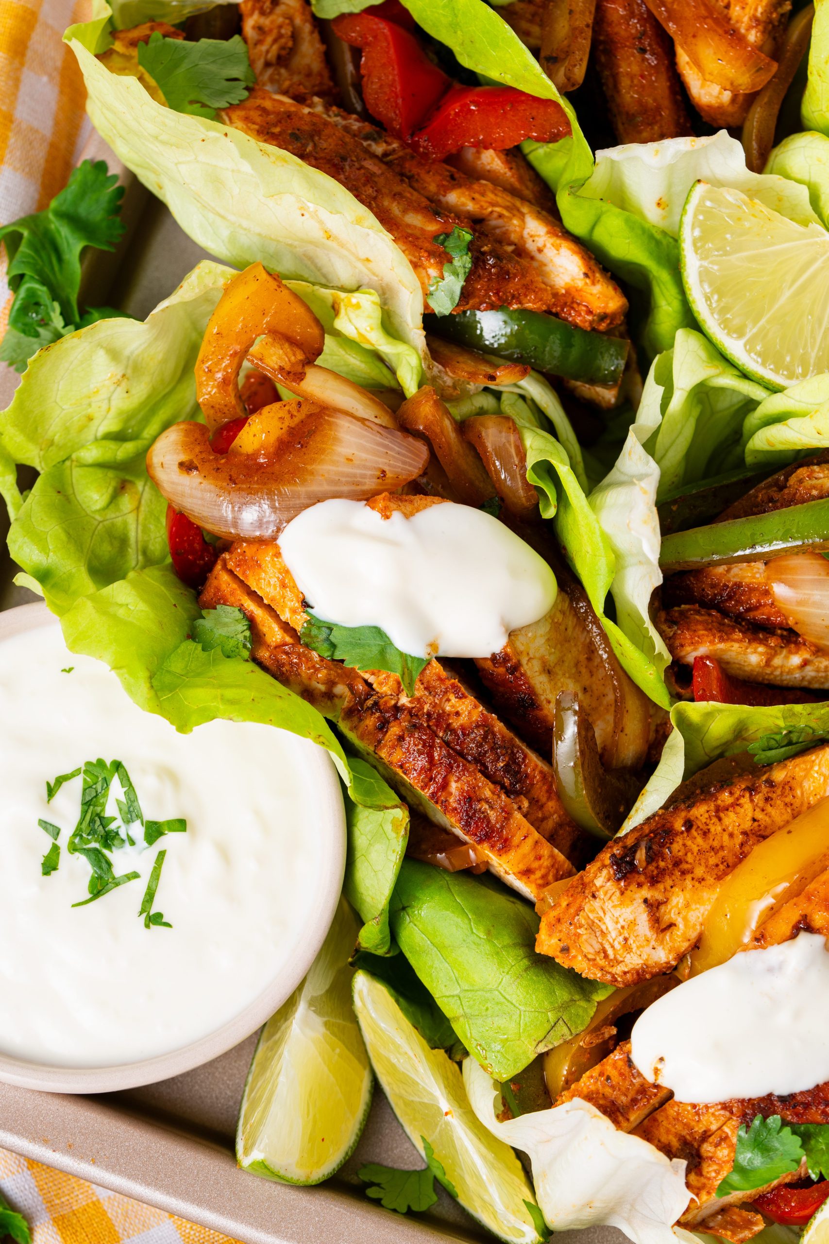 Close-up of multiple lettuce-wrapped chicken fajitas arranged in a tray, filled with chicken, peppers, onions, cilantro, and sour cream.