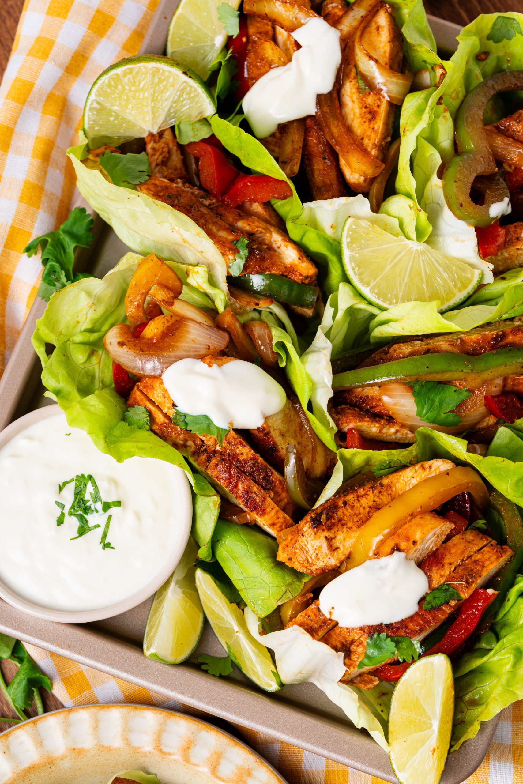 Close-up of multiple lettuce-wrapped chicken fajitas arranged in a tray, filled with chicken, peppers, onions, cilantro, and sour cream.