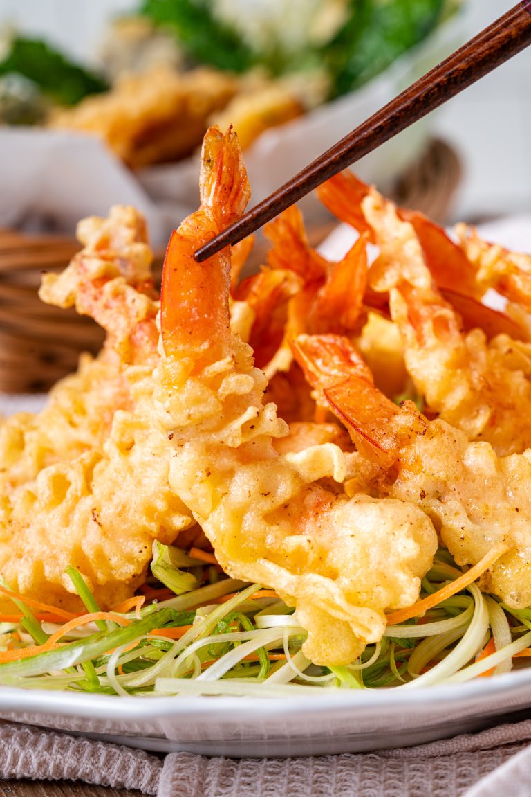 A close-up of crispy shrimp tempura piled high on a plate, showcasing the crunchy batter texture and vibrant orange shrimp tails.