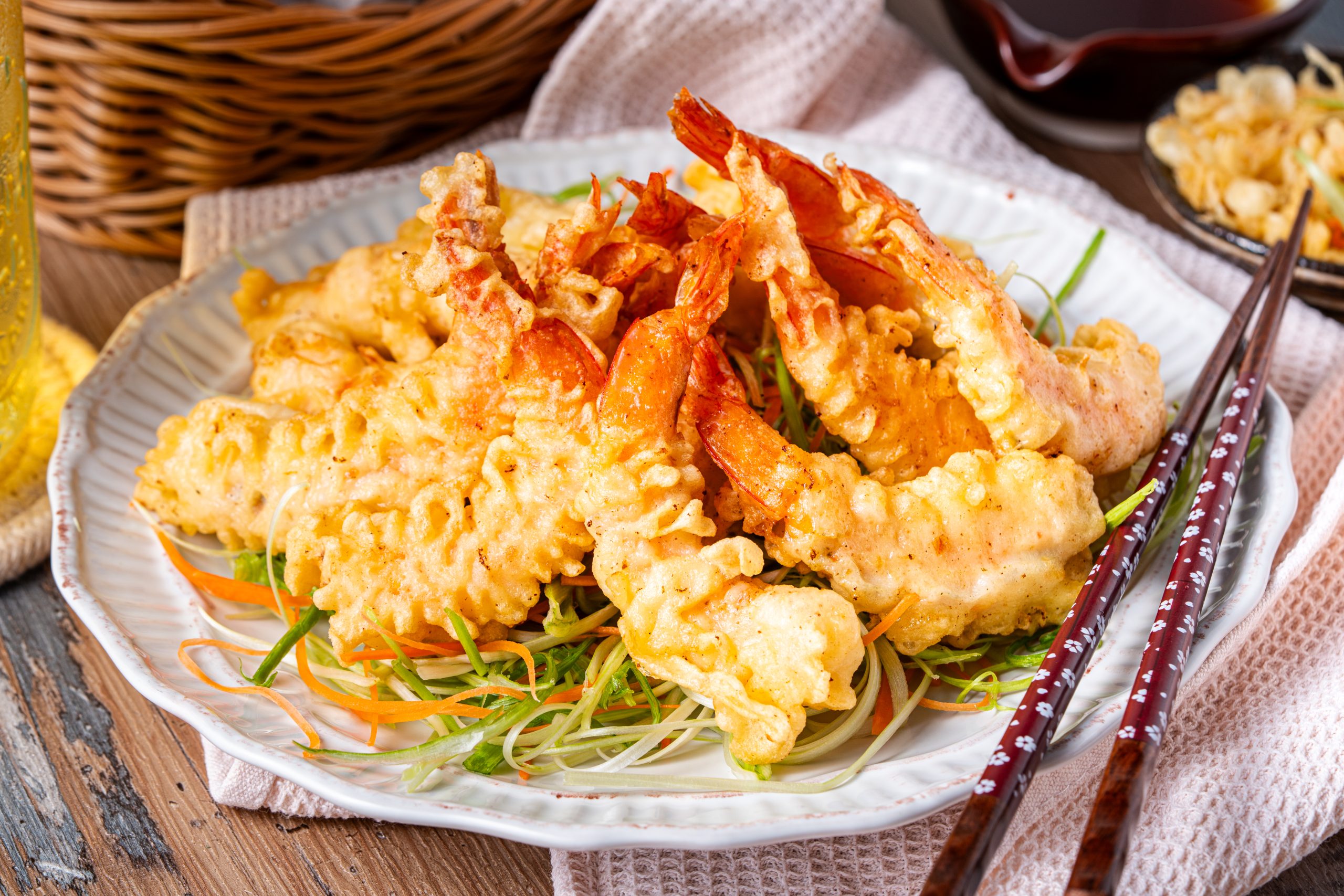 A close-up of crispy shrimp tempura piled high on a plate, showcasing the crunchy batter texture and vibrant orange shrimp tails.