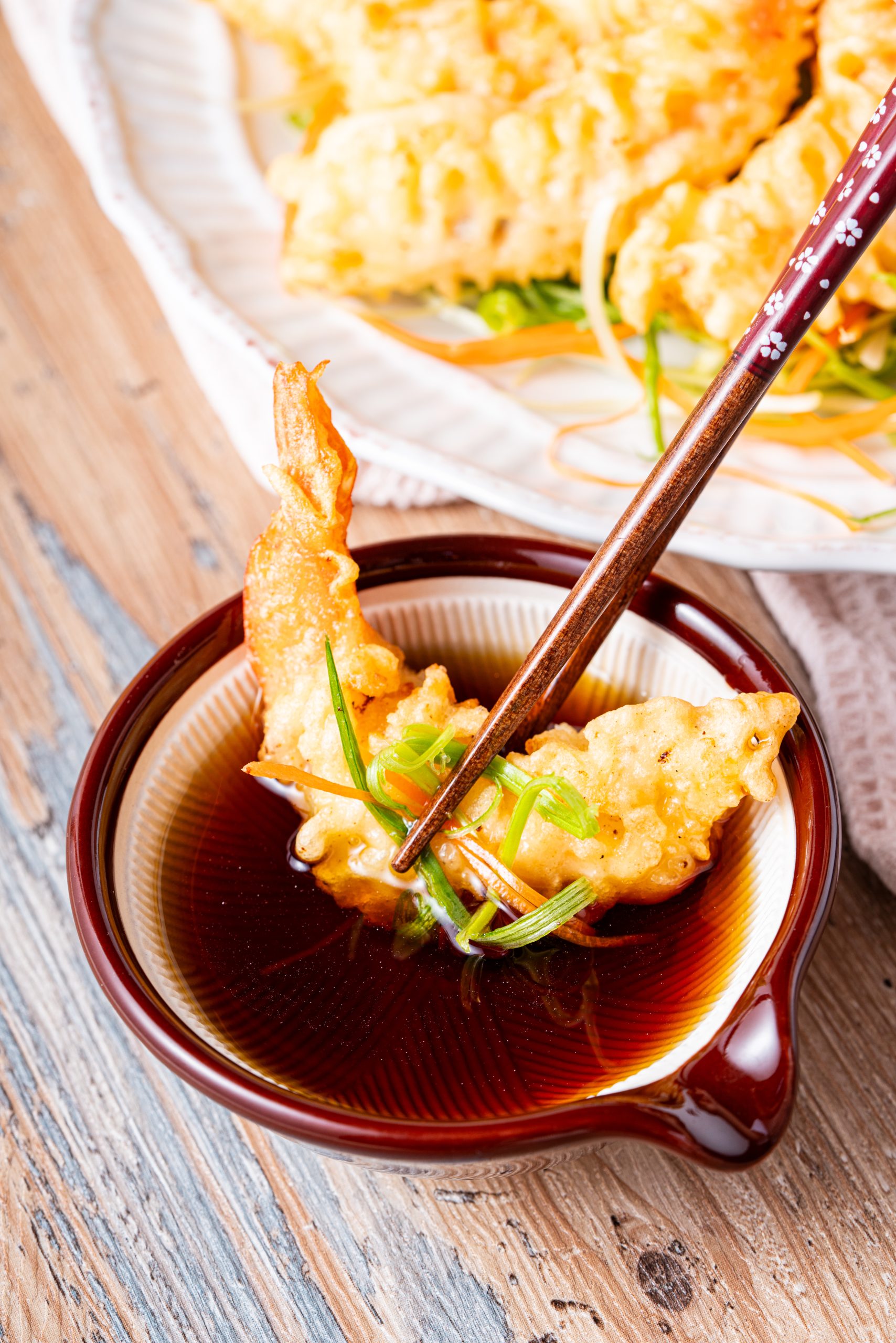 A close-up of crispy shrimp tempura piled high on a plate, showcasing the crunchy batter texture and vibrant orange shrimp tails.