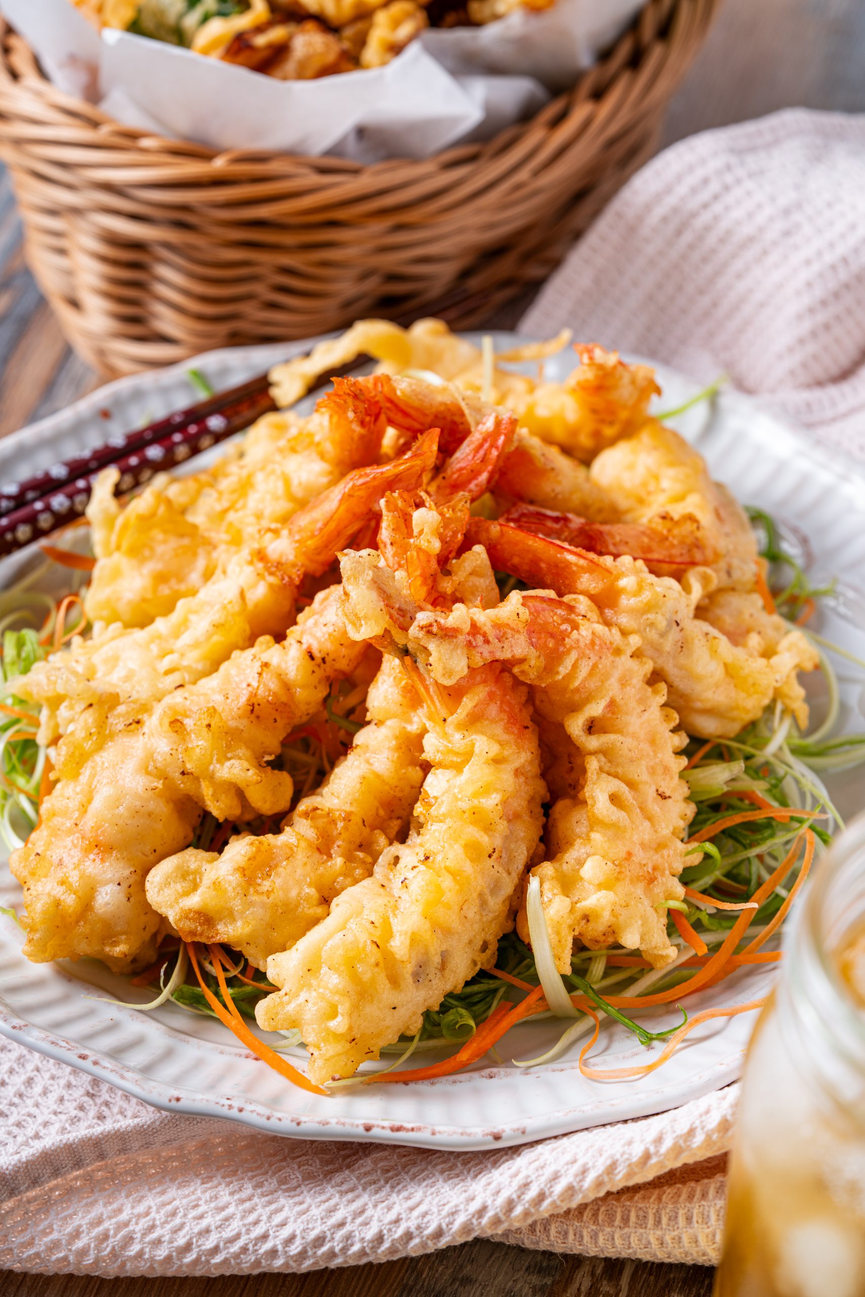 A close-up of crispy shrimp tempura piled high on a plate, showcasing the crunchy batter texture and vibrant orange shrimp tails.
