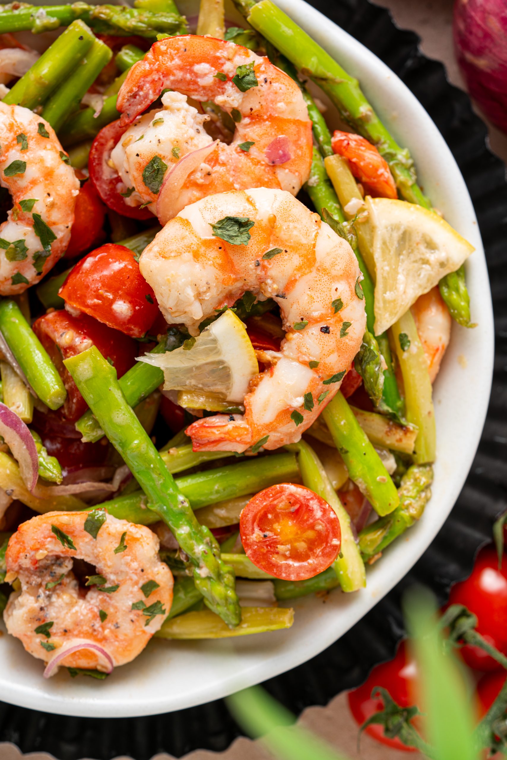 Close-up of juicy shrimp tossed with tender asparagus spears, cherry tomatoes, and herbs in a warm asparagus and shrimp salad.