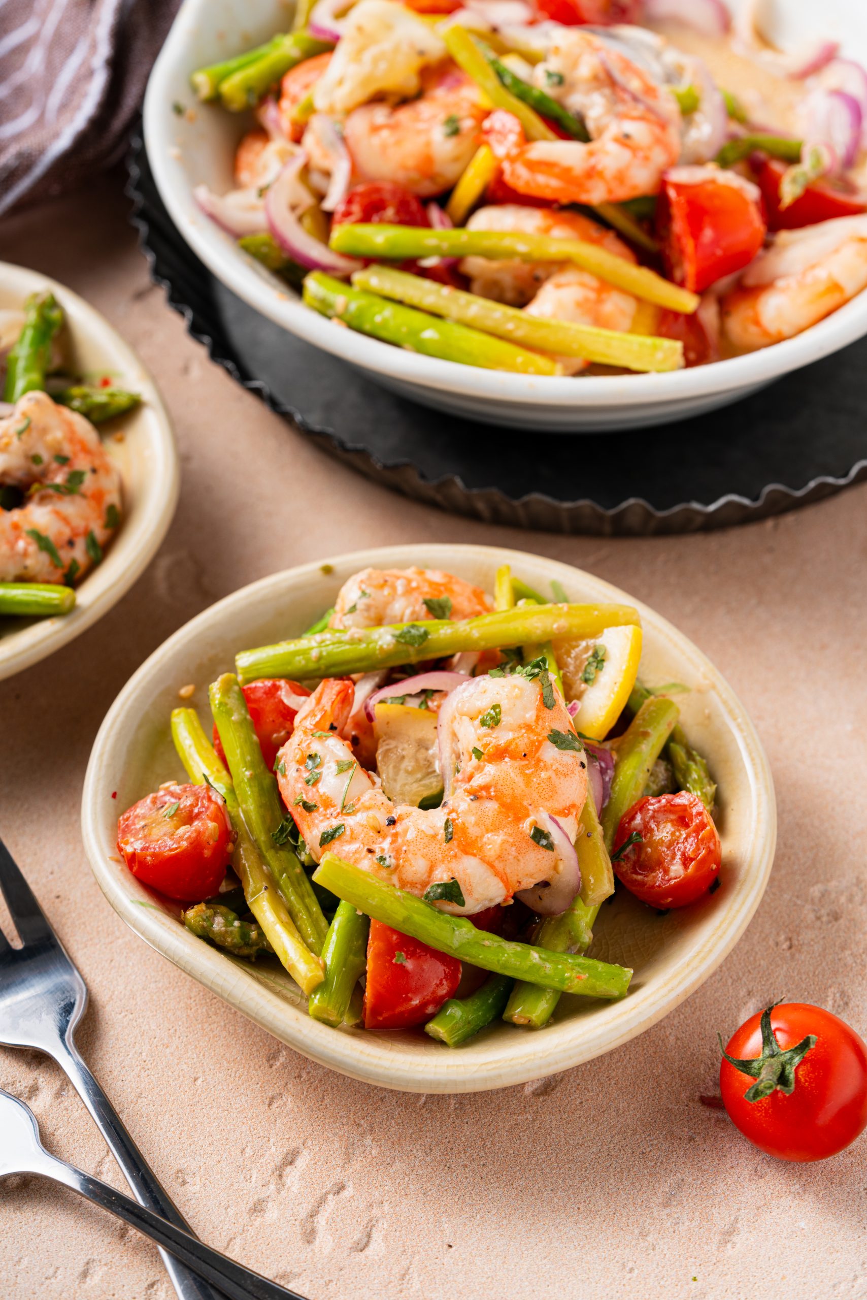 Warm asparagus and shrimp salad served in small dishes, garnished with herbs and fresh lemon, with tomatoes and utensils on the side.