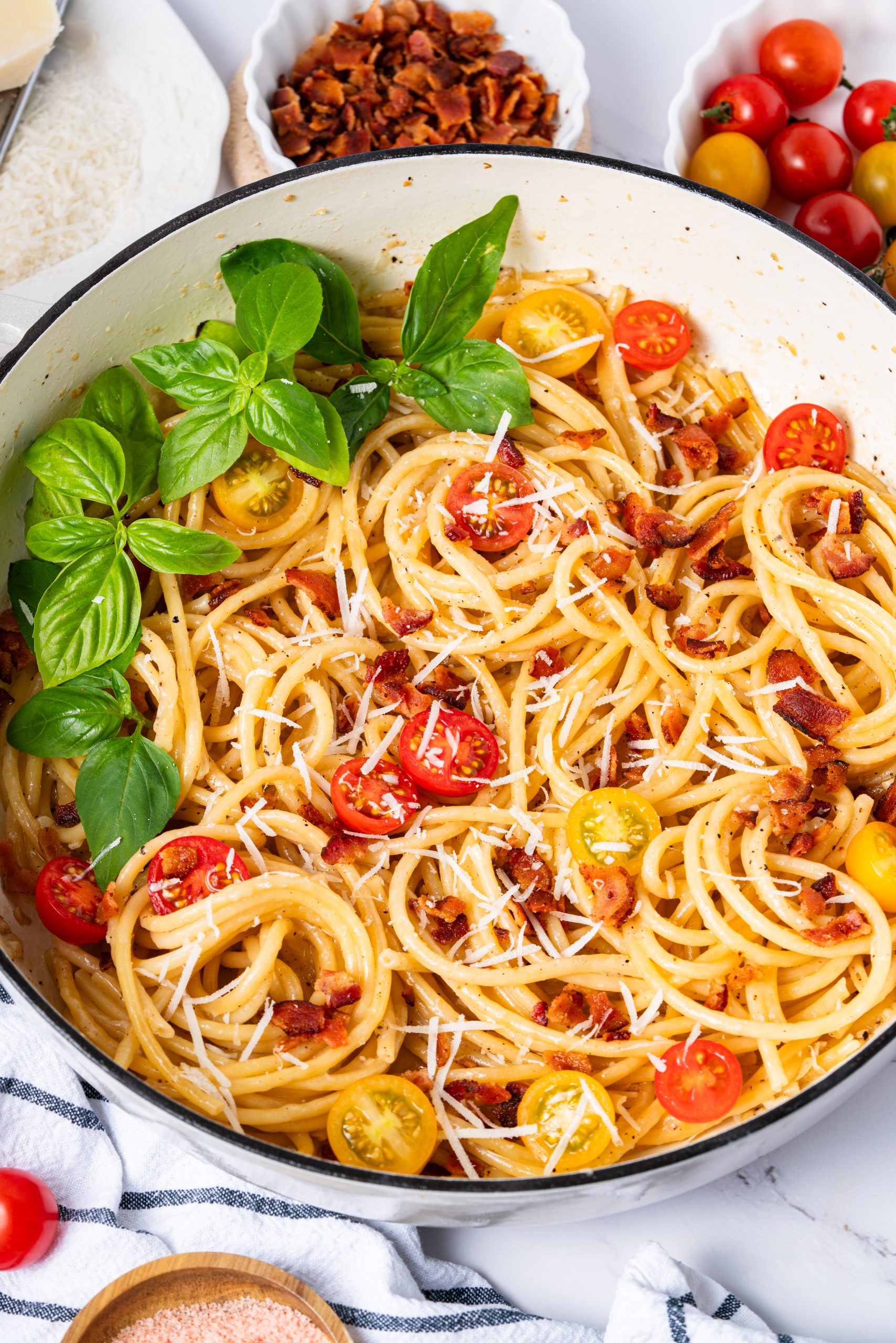 Overhead view of Cacio e Pepe pasta with cracked black pepper, grated cheese, cherry tomatoes, and basil leaves in a white pan.
