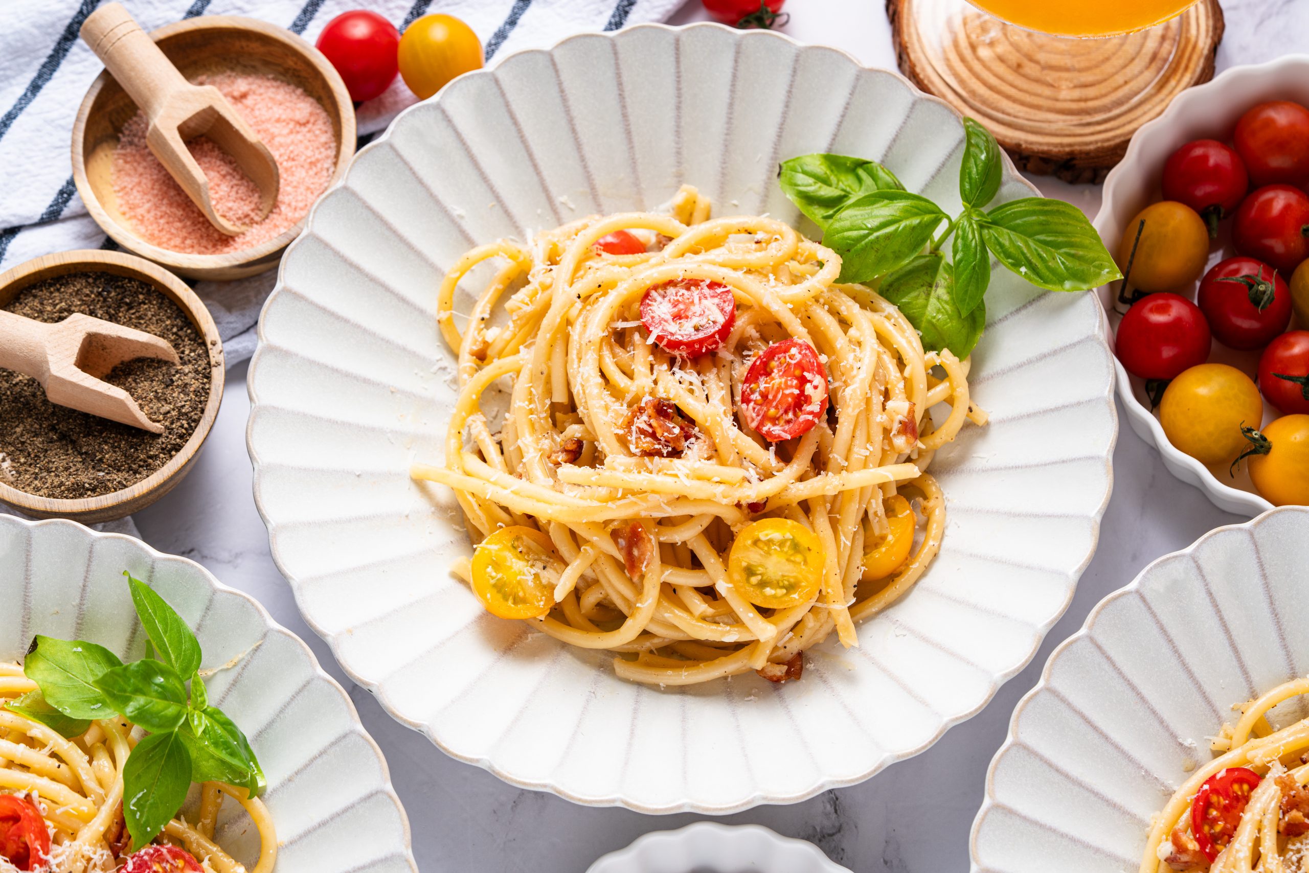 Flat lay of Cacio e Pepe Italian pasta with spaghetti, Pecorino Romano cheese, black pepper, tomatoes, and fresh herbs.