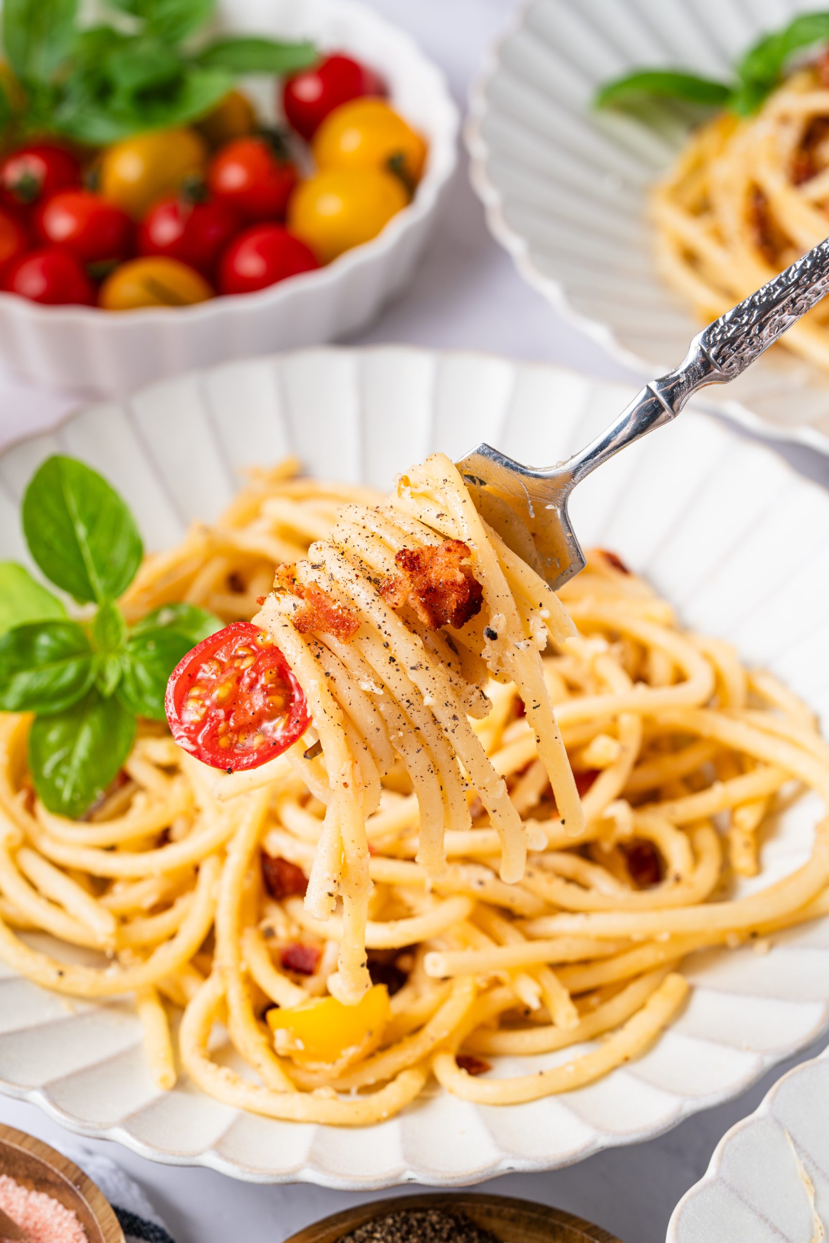 Fork lifting a bite of Cacio e Pepe spaghetti with black pepper, cheese shavings, and cherry tomato.