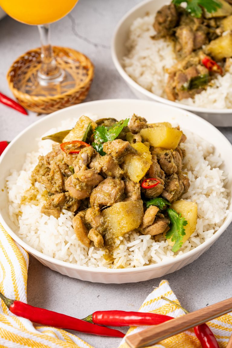 Bowl of Thai green curry chicken served over white rice, garnished with fresh cilantro and red chili.