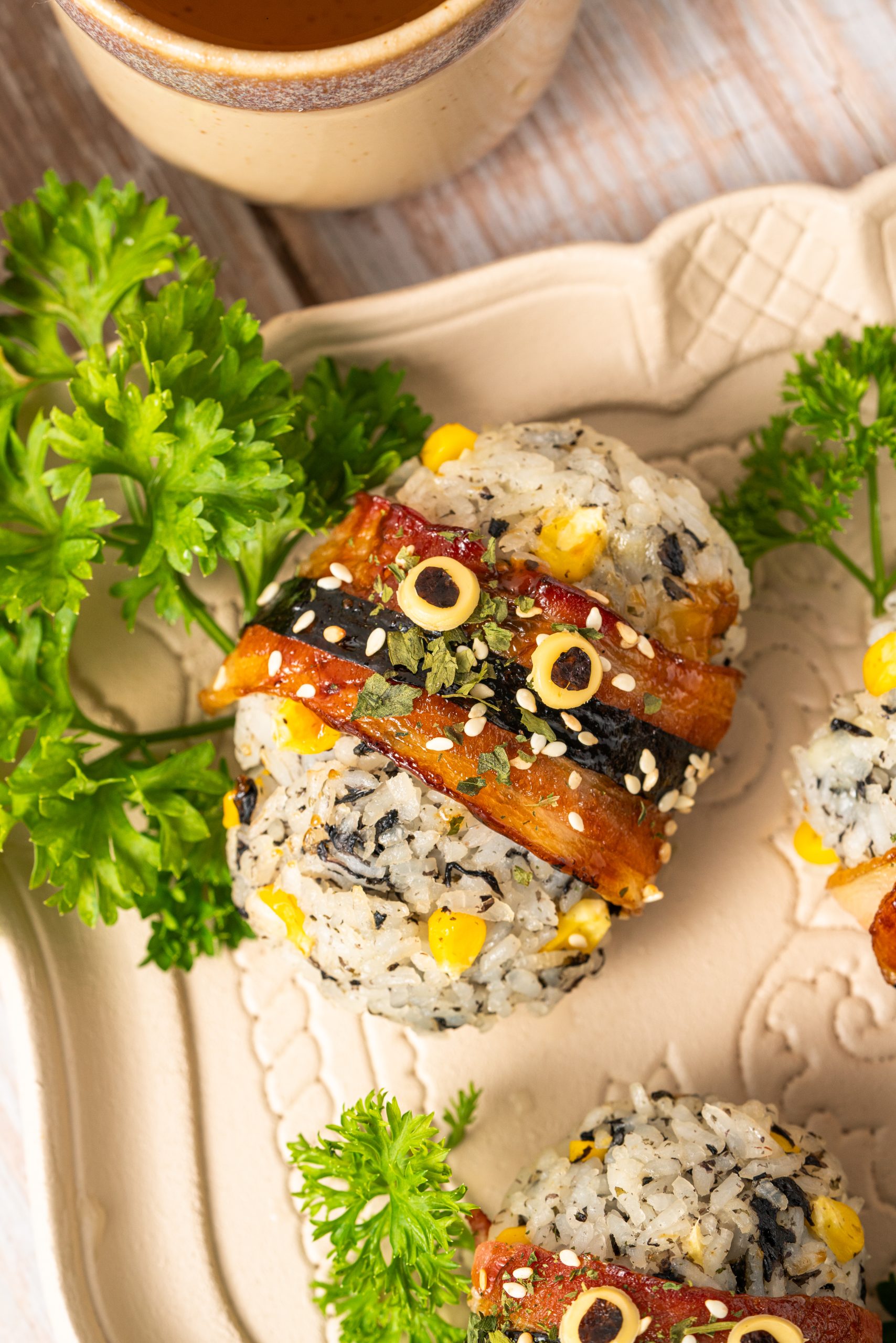 Bacon-wrapped rice balls topped with sesame seeds and nori, featuring crispy glazed bacon over seasoned rice with corn, garnished with fresh parsley.