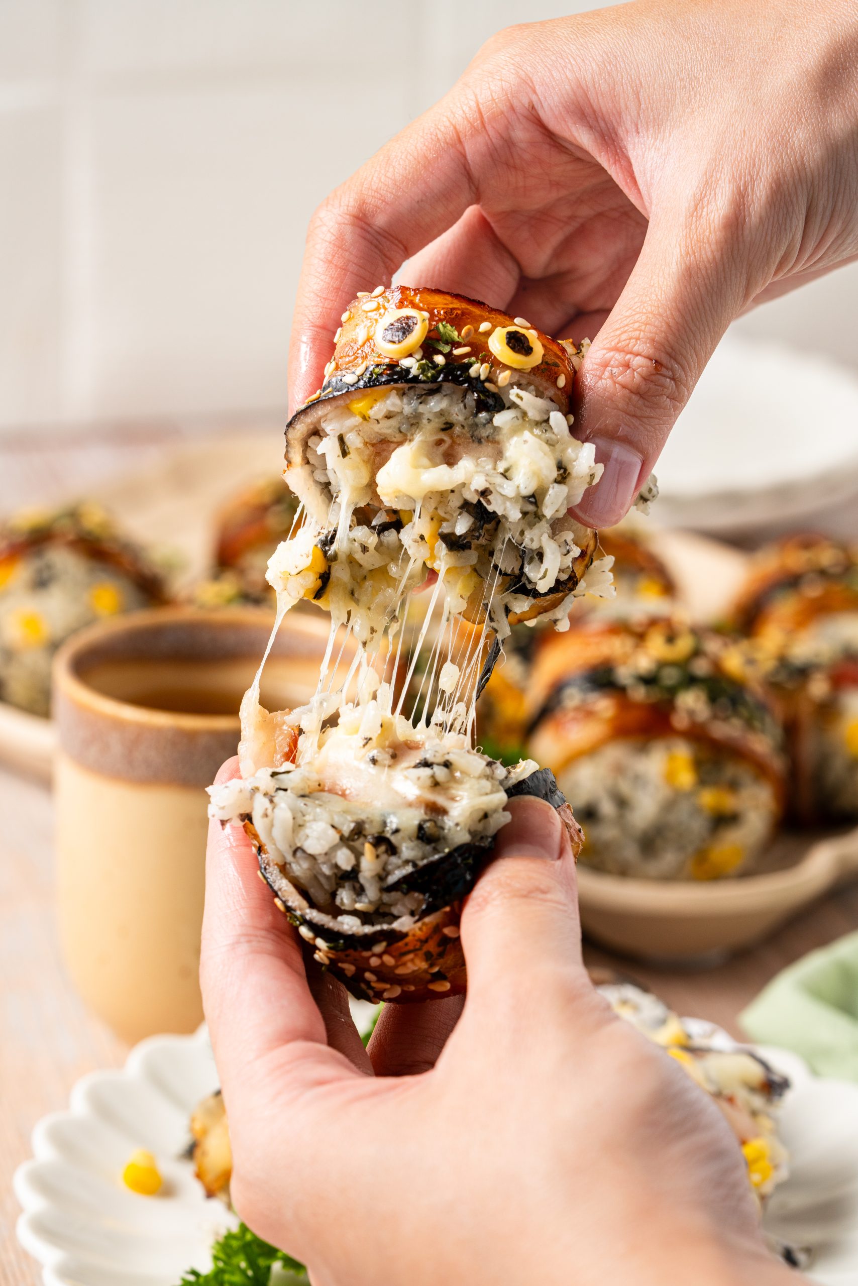 Hands pulling apart a bacon-wrapped rice ball with melted cheese stretching from the center