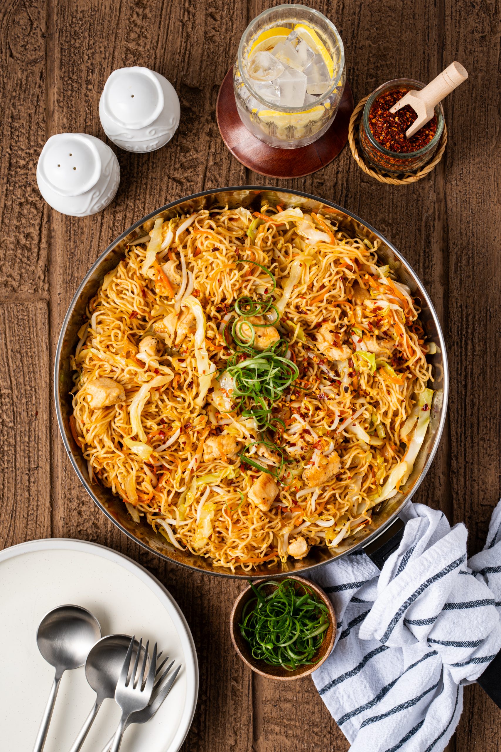 Ramen noodle stir fry with chicken, cabbage, carrots, and green onions served in a skillet on a rustic wooden table