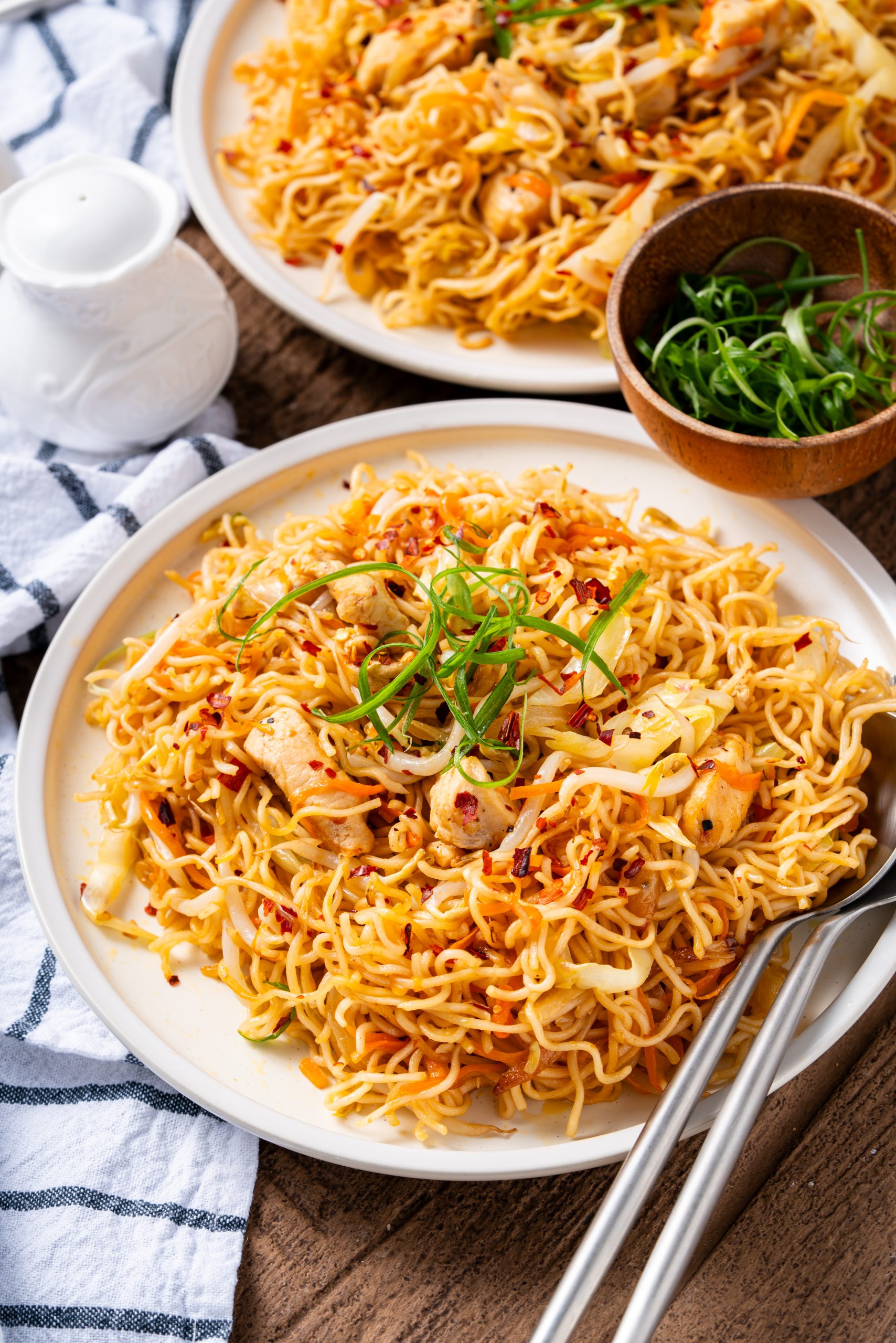 Chicken ramen noodle stir fry served on a white plate with chopsticks and fresh scallions