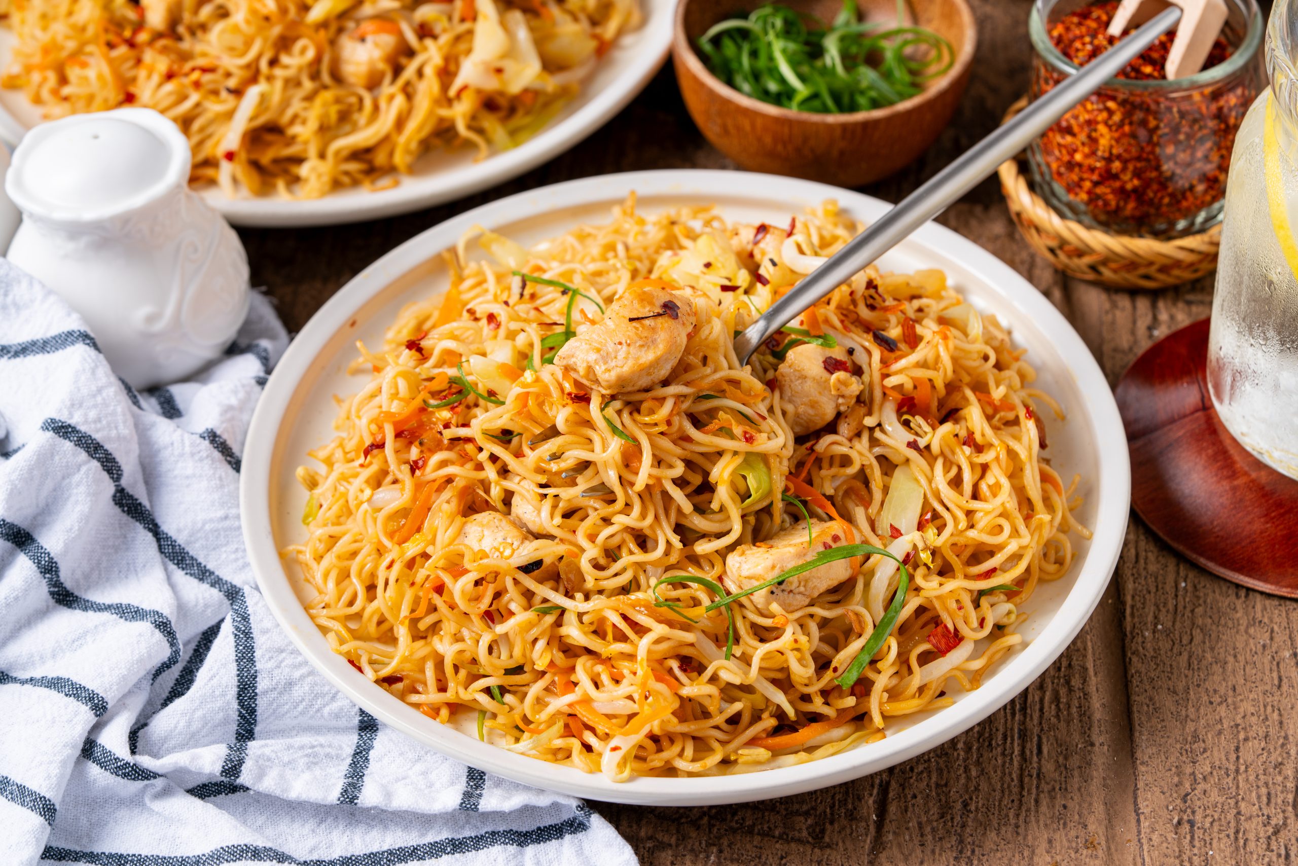 Ramen noodle stir fry with chicken served family-style with fresh green onions and chili flakes