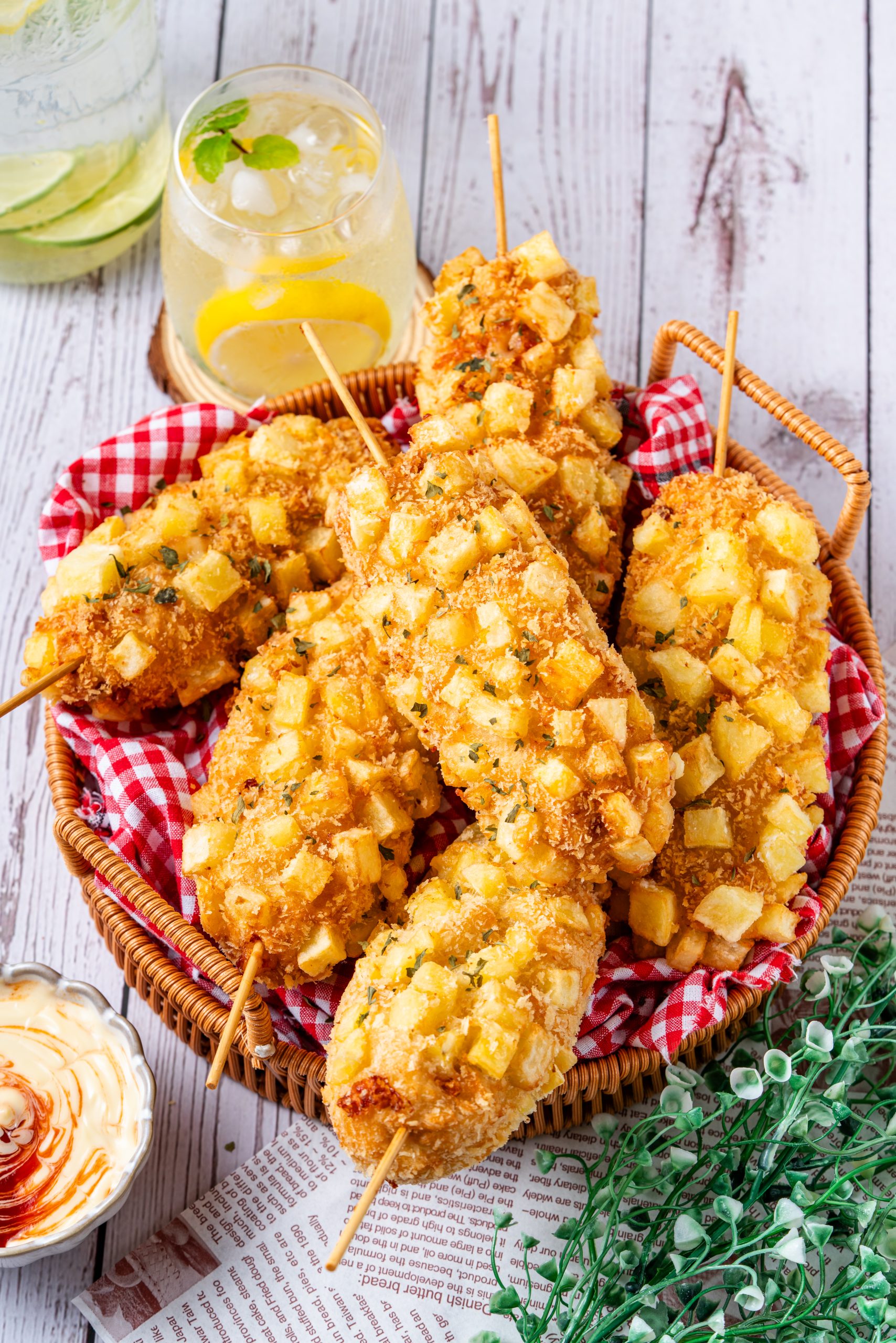 Golden Korean potato corn dogs on sticks, crunchy outside with fluffy interior, served in a basket with lemonade and creamy dipping sauce.