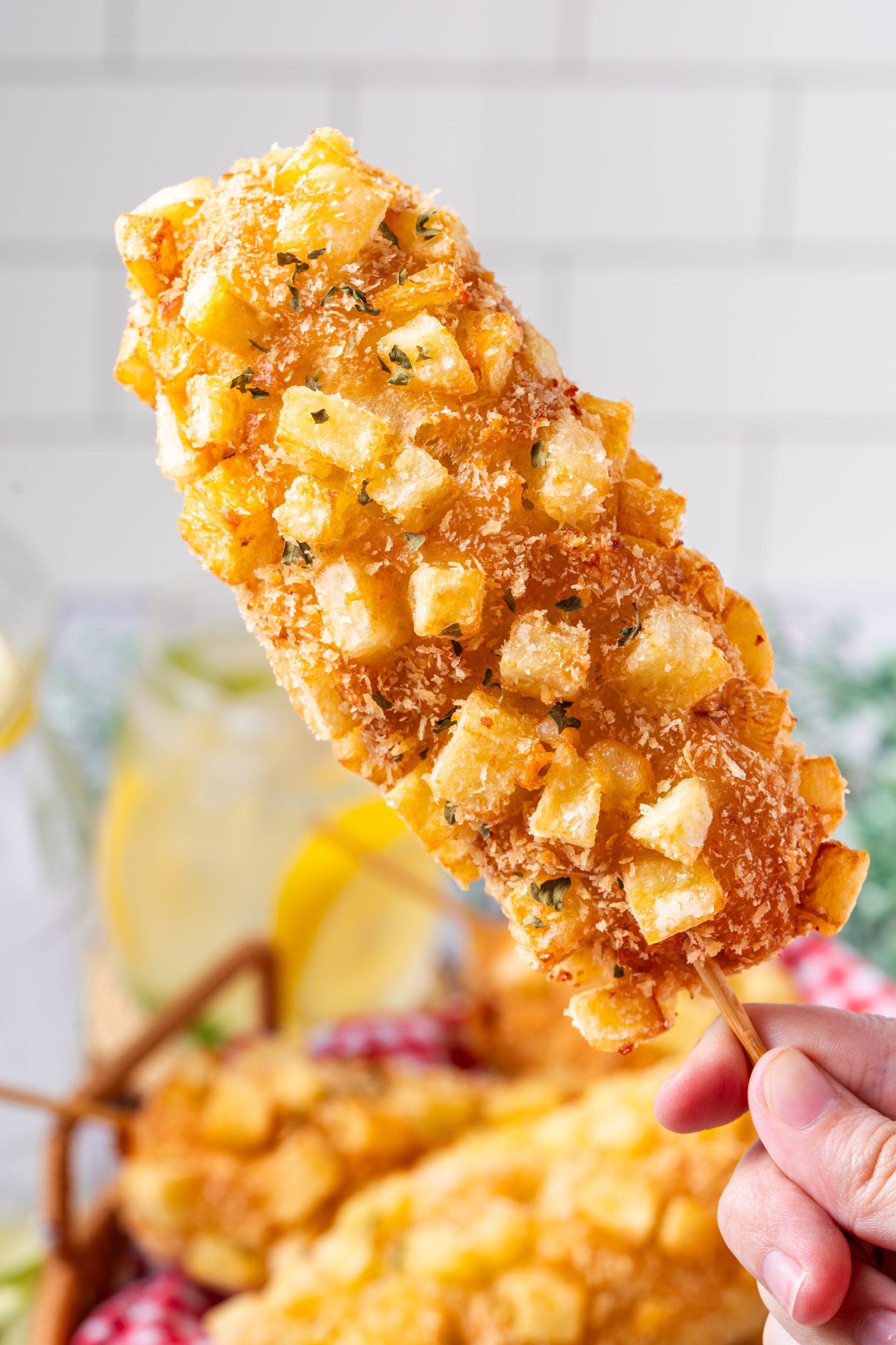 Close-up of a Korean potato corn dog showing golden, crunchy potato crust with herbs and flaky coating.