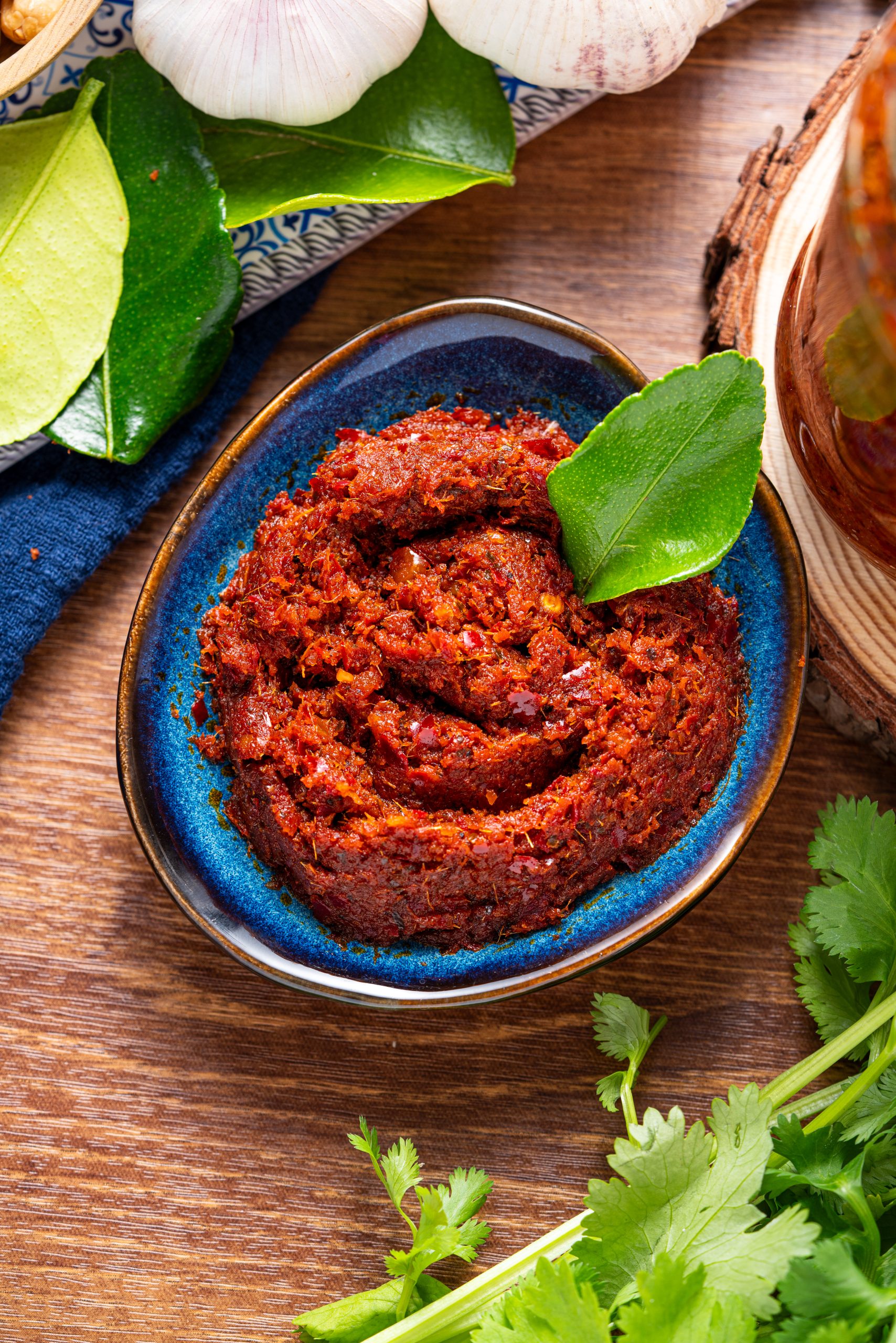 Close-up of homemade Panang curry paste in blue bowl garnished with kaffir lime leaf.