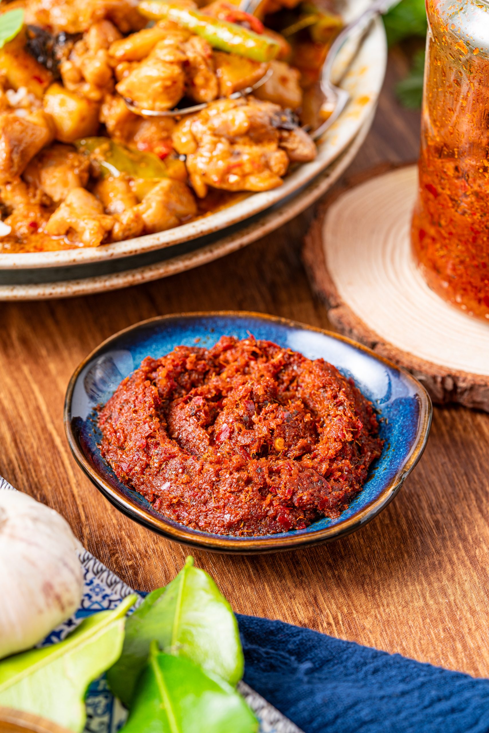 Panang curry paste in a blue bowl with kaffir lime leaves, served alongside chicken curry and fresh Thai herbs – authentic homemade Thai red curry paste.