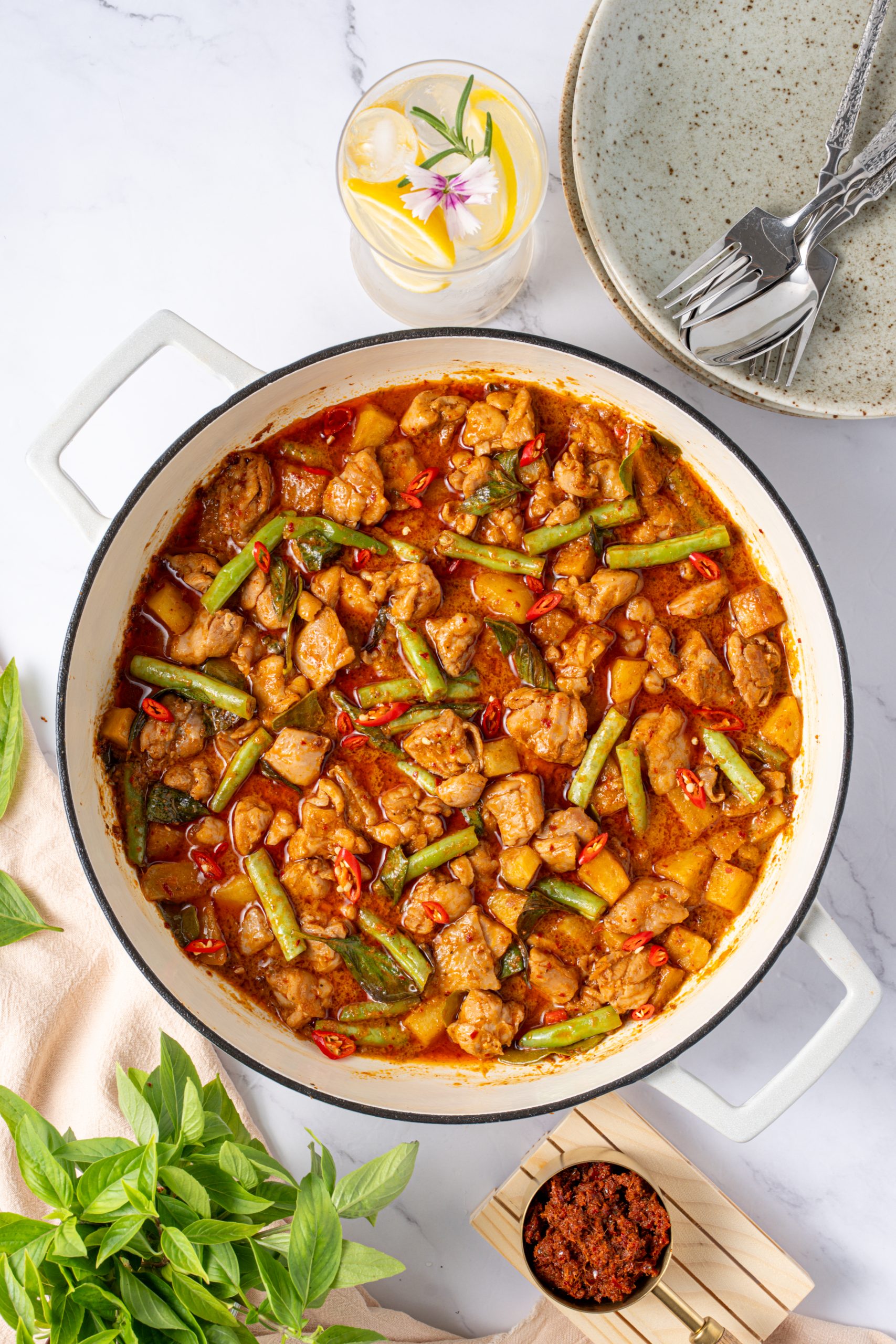 Thai chicken Panang curry in a white skillet, simmered in rich coconut red curry sauce with green beans, potatoes, chili slices and fresh basil – authentic homemade Panang curry recipe.
