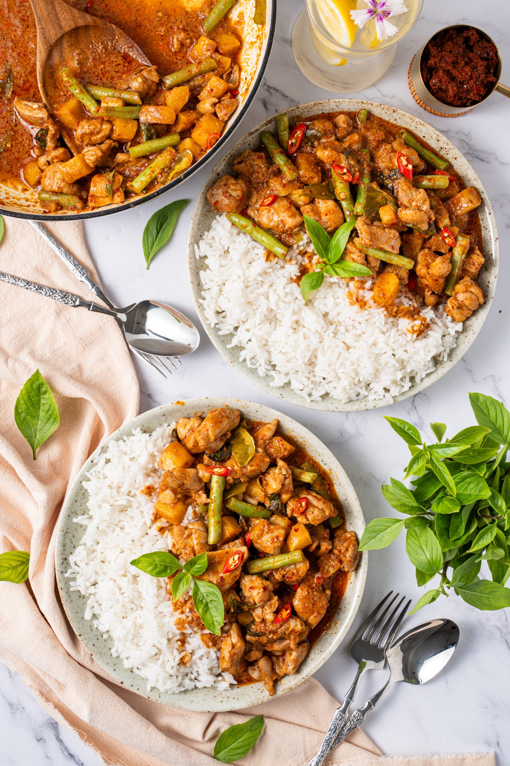 Overhead view of chicken Panang curry and rice bowls, rich Thai coconut curry with chicken, green beans, and basil served alongside steamed jasmine rice.