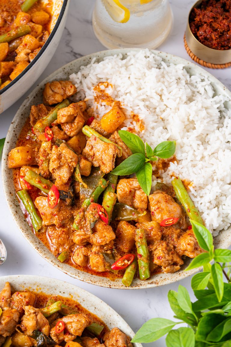 Bowl of chicken Panang curry with jasmine rice, topped with fresh Thai basil and red chili, served with steamed white rice for a classic Thai dinner.