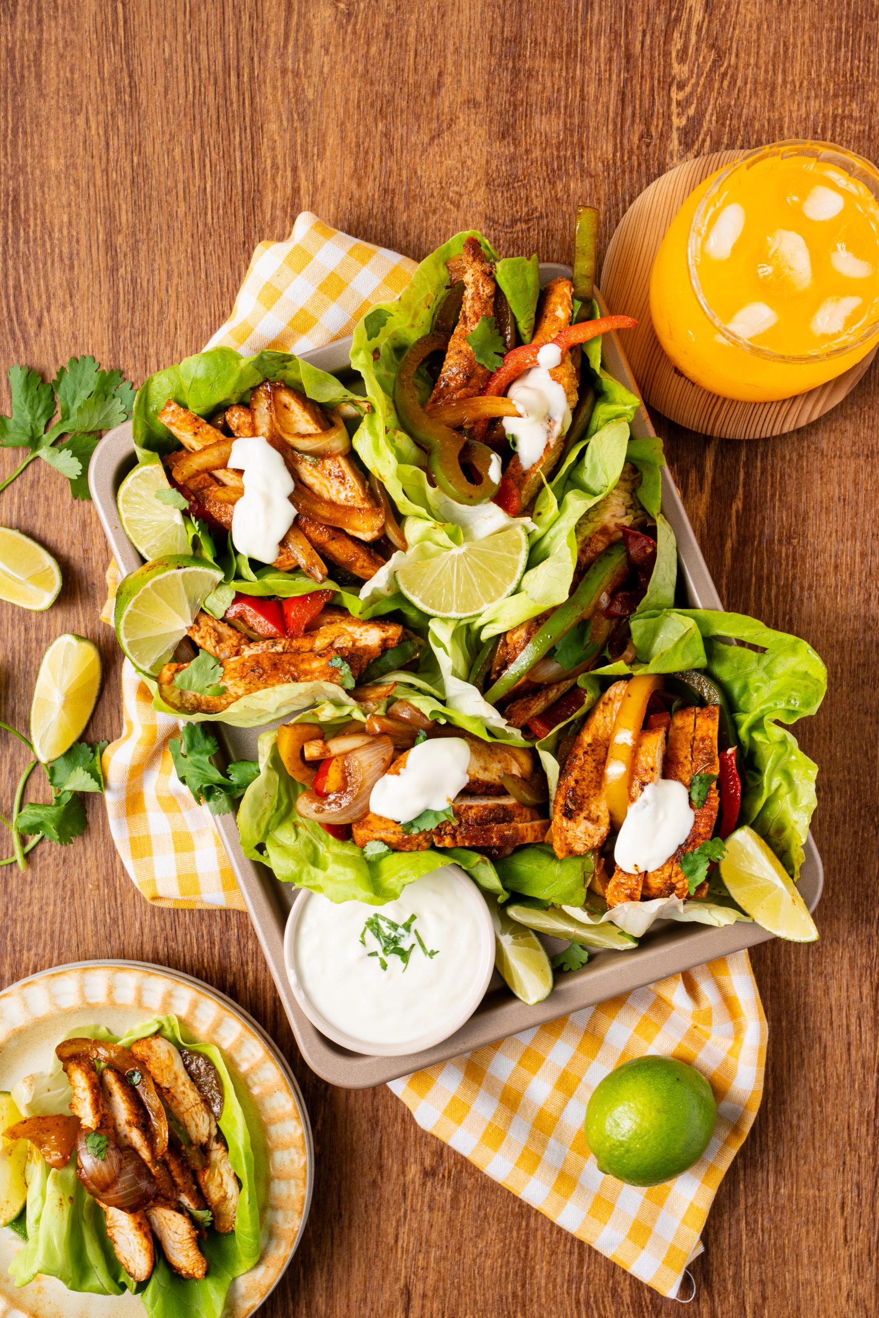 Overhead of multiple lettuce-wrapped chicken fajitas arranged in a tray, filled with chicken, peppers, onions, cilantro, and sour cream.