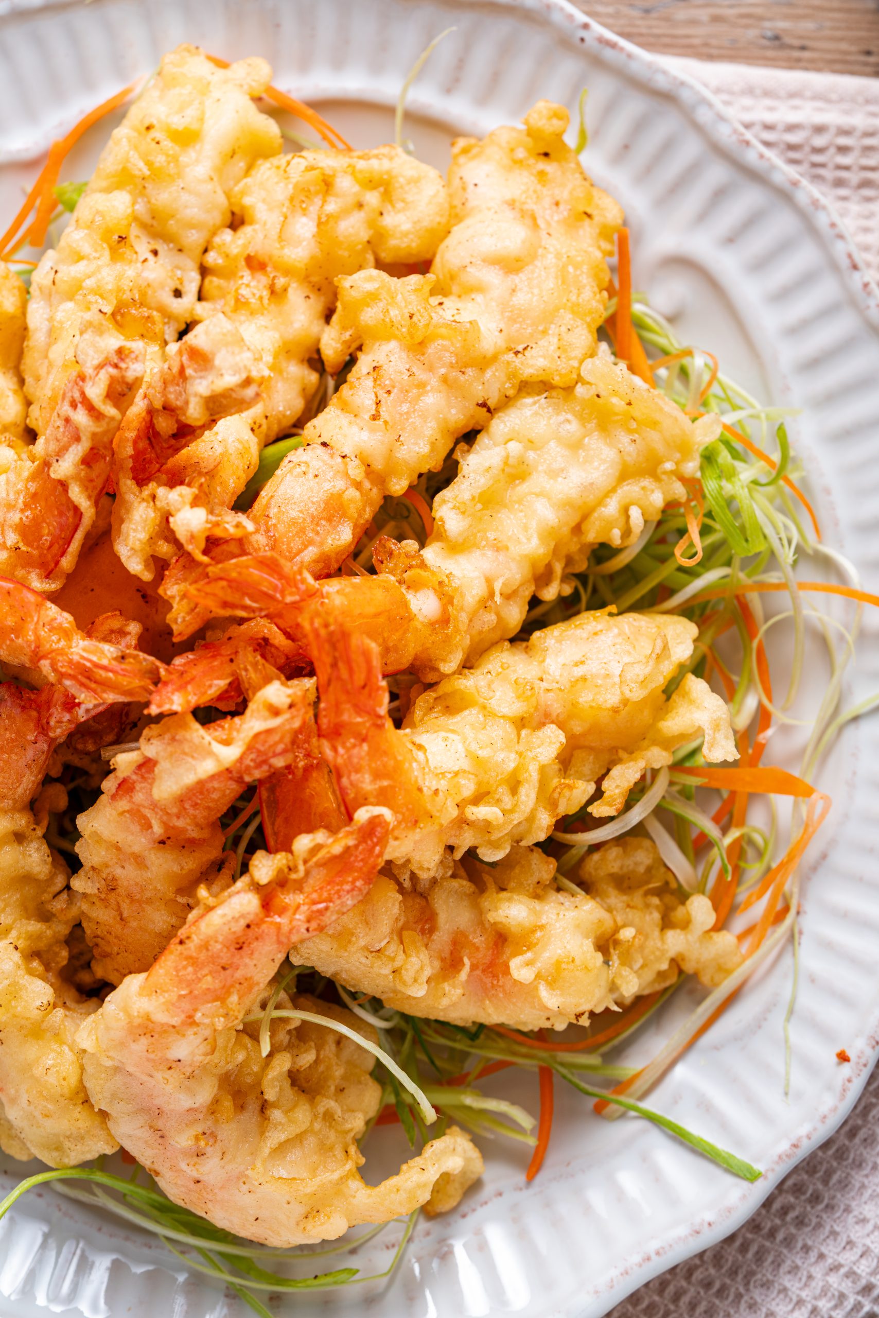 A overhead shot of golden, crispy shrimp tempura arranged on a bed of thinly sliced carrots and green onions