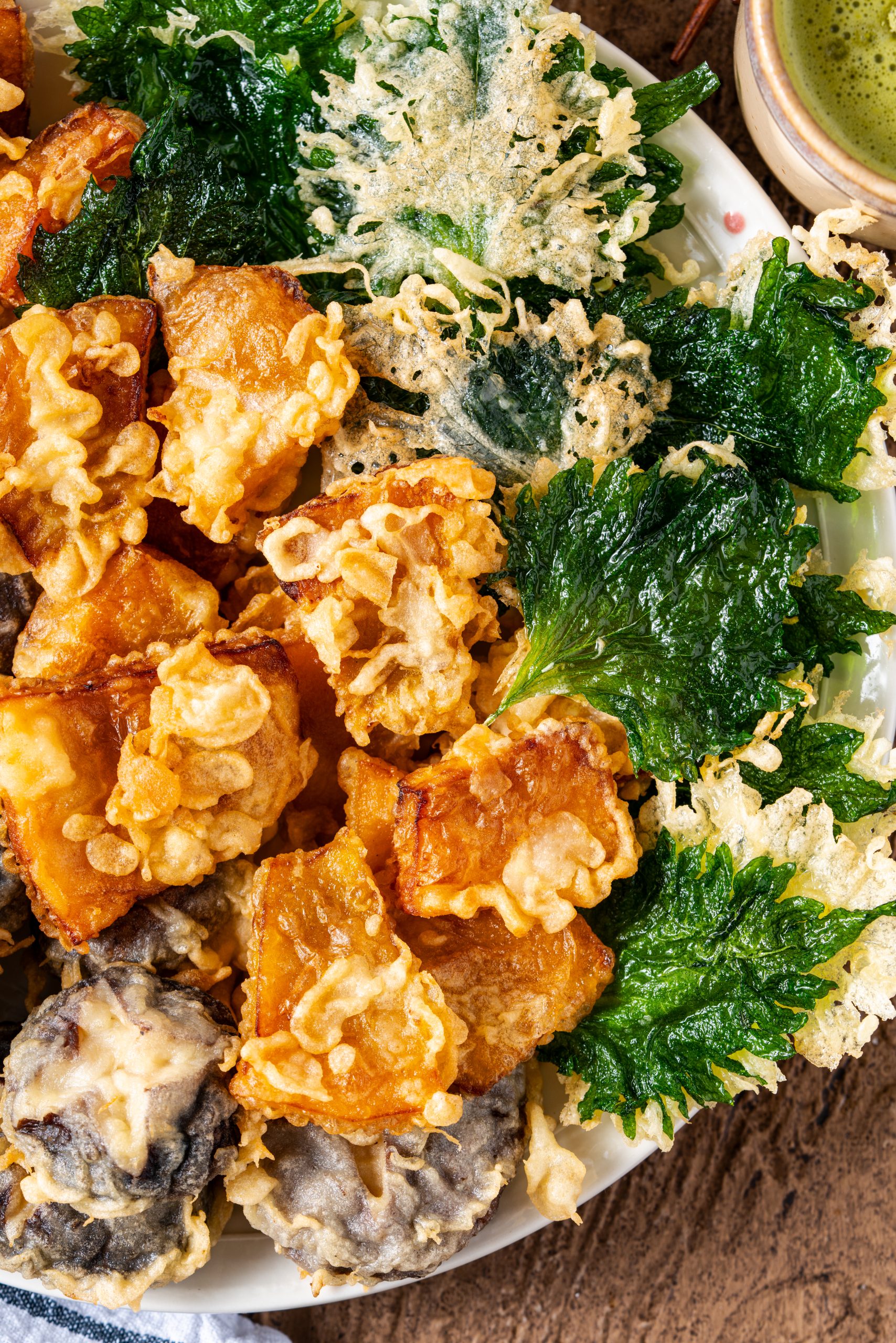 Crispy vegetable tempura platter with golden sliced pumpkin, mushrooms, and shiso leaves served with dipping sauce and grated daikon.