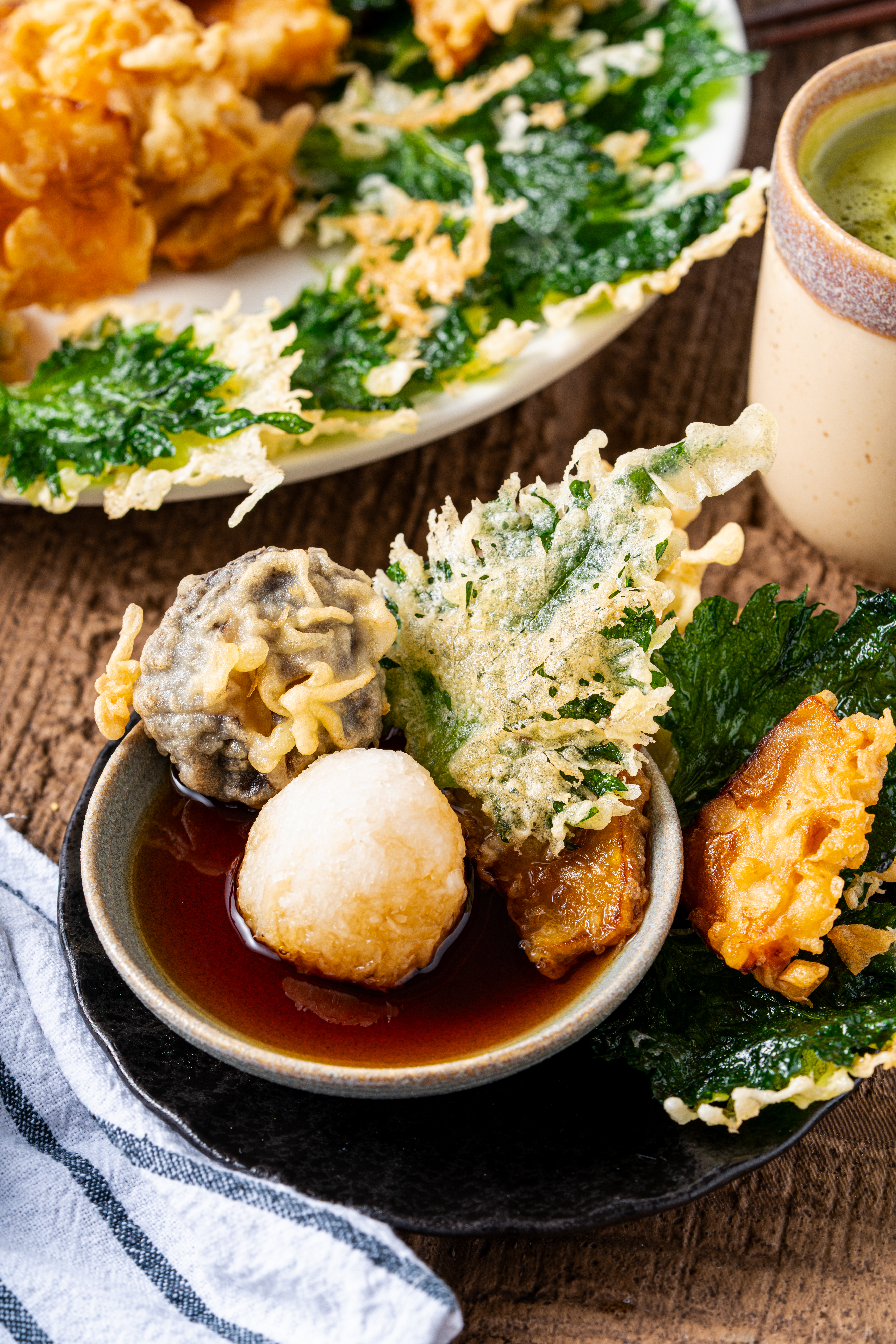 Vegetable tempura dipped in soy-based sauce with grated daikon, showcasing crispy Japanese tempura texture.