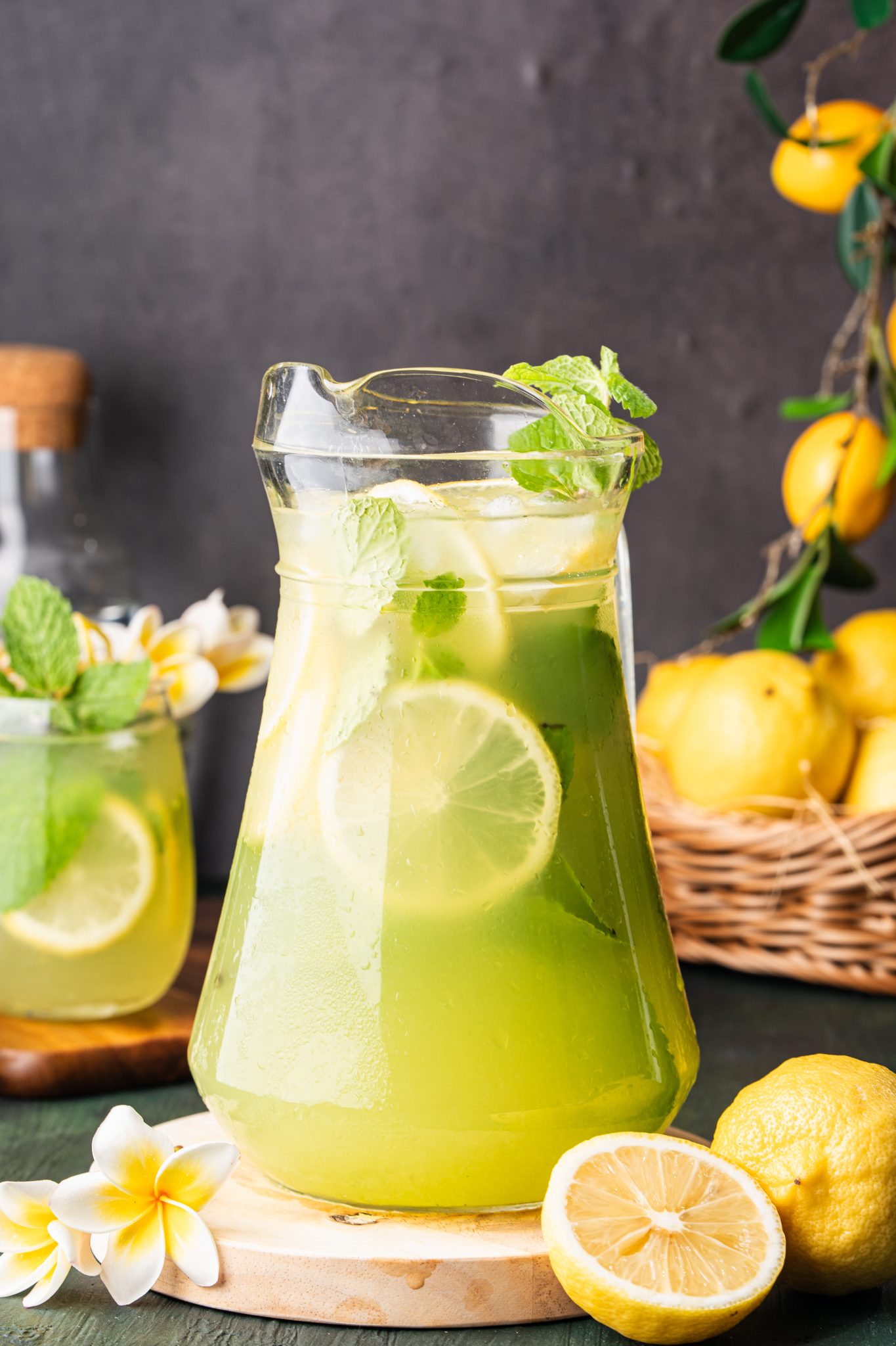 Pitcher of refreshing cucumber lemonade with lemon slices, mint, and ice, styled with fresh lemons and flowers.