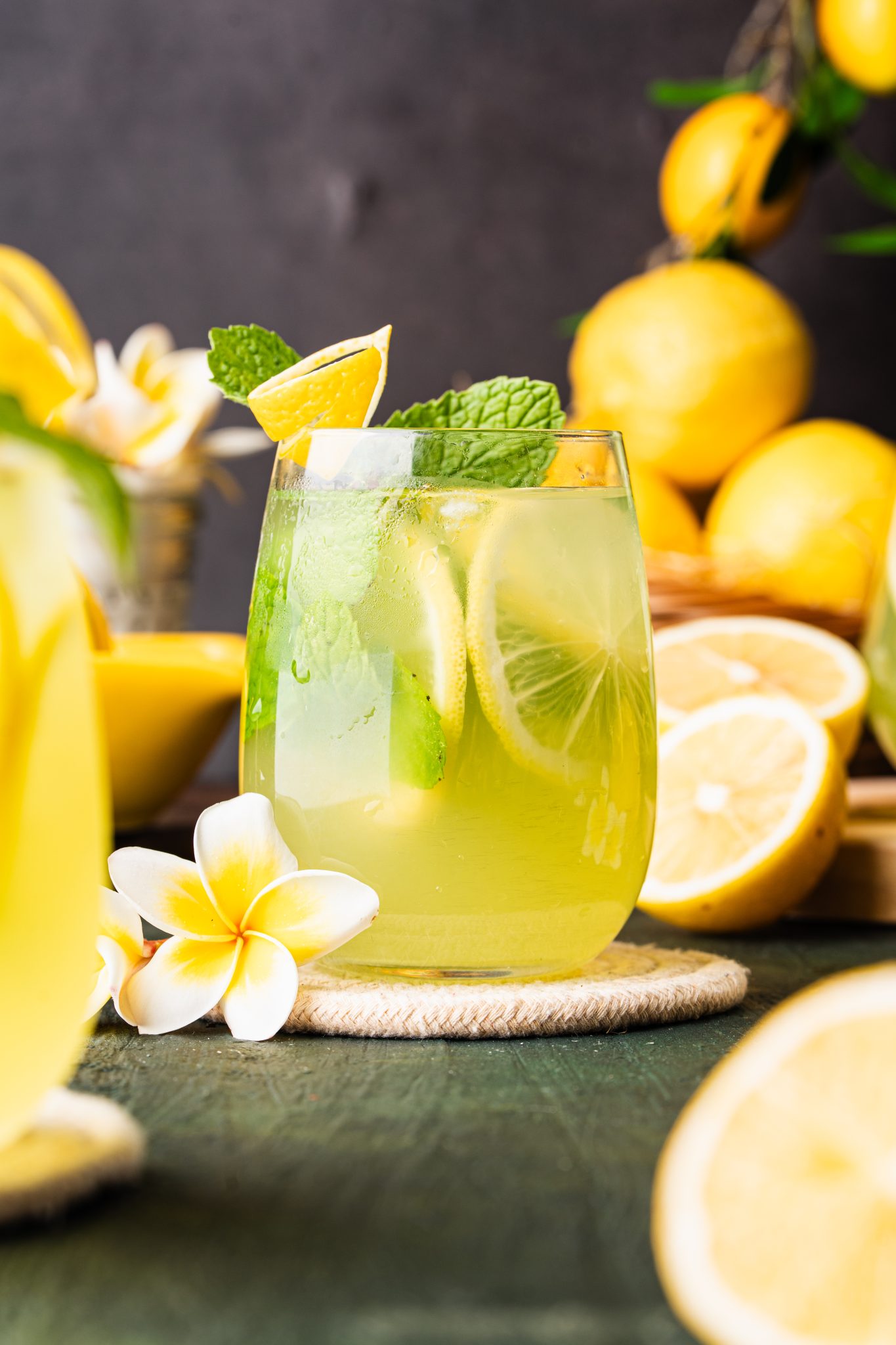 Refreshing cucumber lemonade in a glass with lemon slices, mint, and ice on a dark green surface.