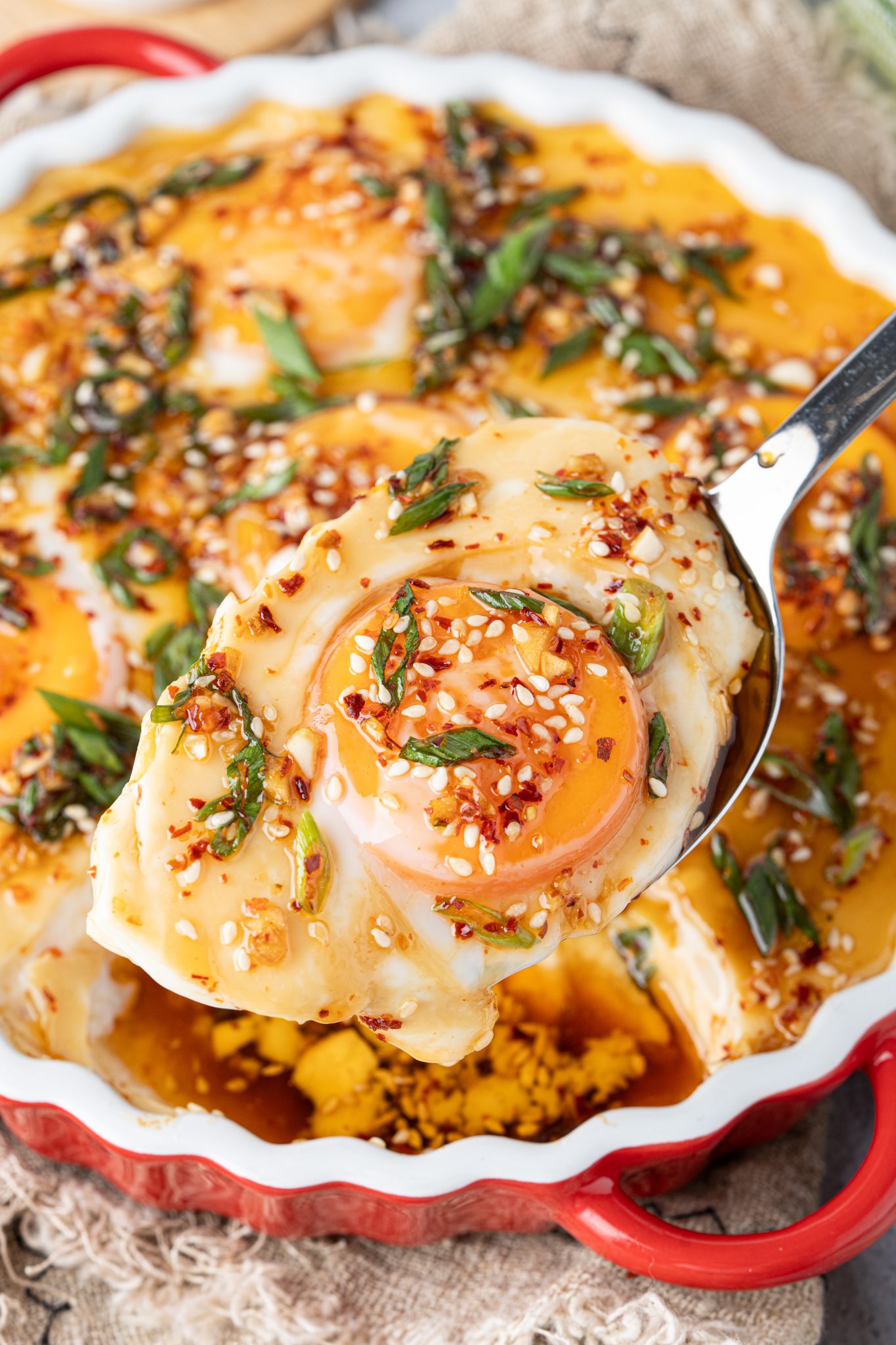 Spoon lifting a serving of silky double steamed eggs with a soft egg yolk and spicy chili garlic topping.