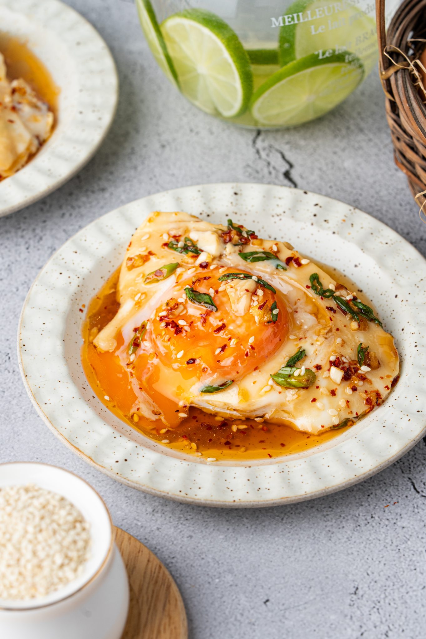 Slice of silky steamed egg custard with runny yolks on a plate with chili oil, sesame seeds, and fresh scallions.