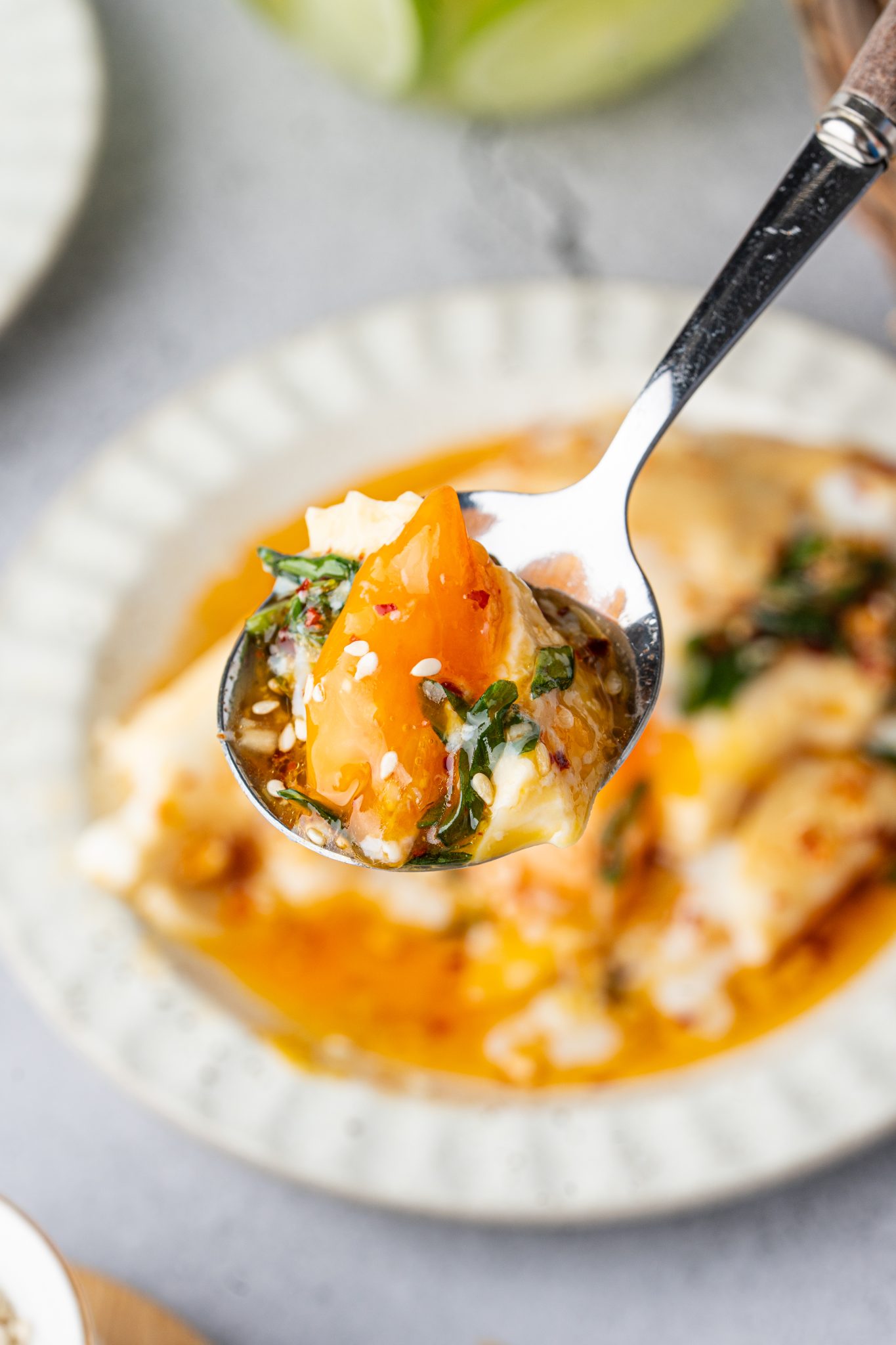 Spoonful of creamy Chinese double steamed eggs with runny egg yolk, chili oil, sesame seeds, and scallions.