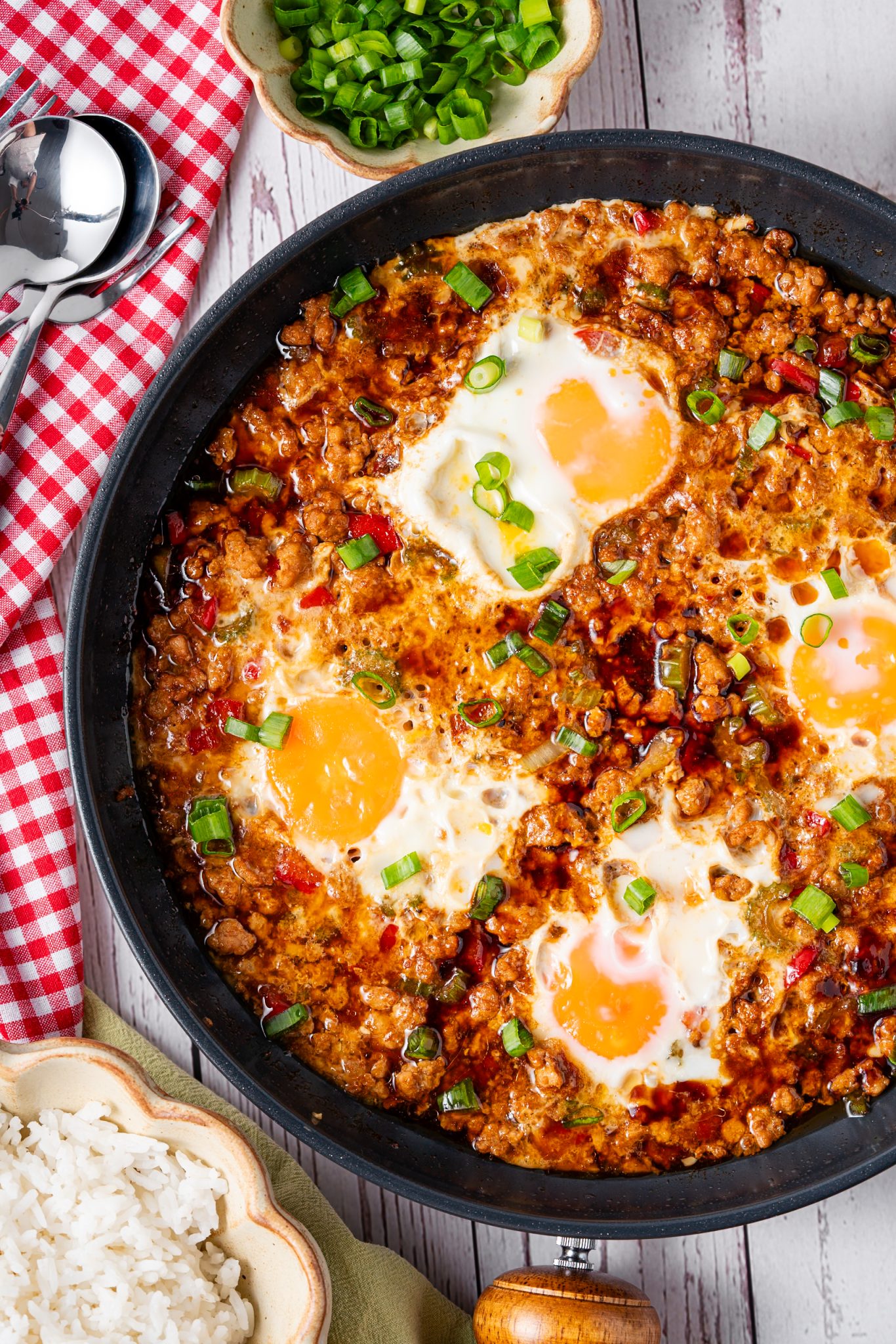 Skillet of saucy minced meat and fried eggs topped with scallions, served with white rice on the side.
