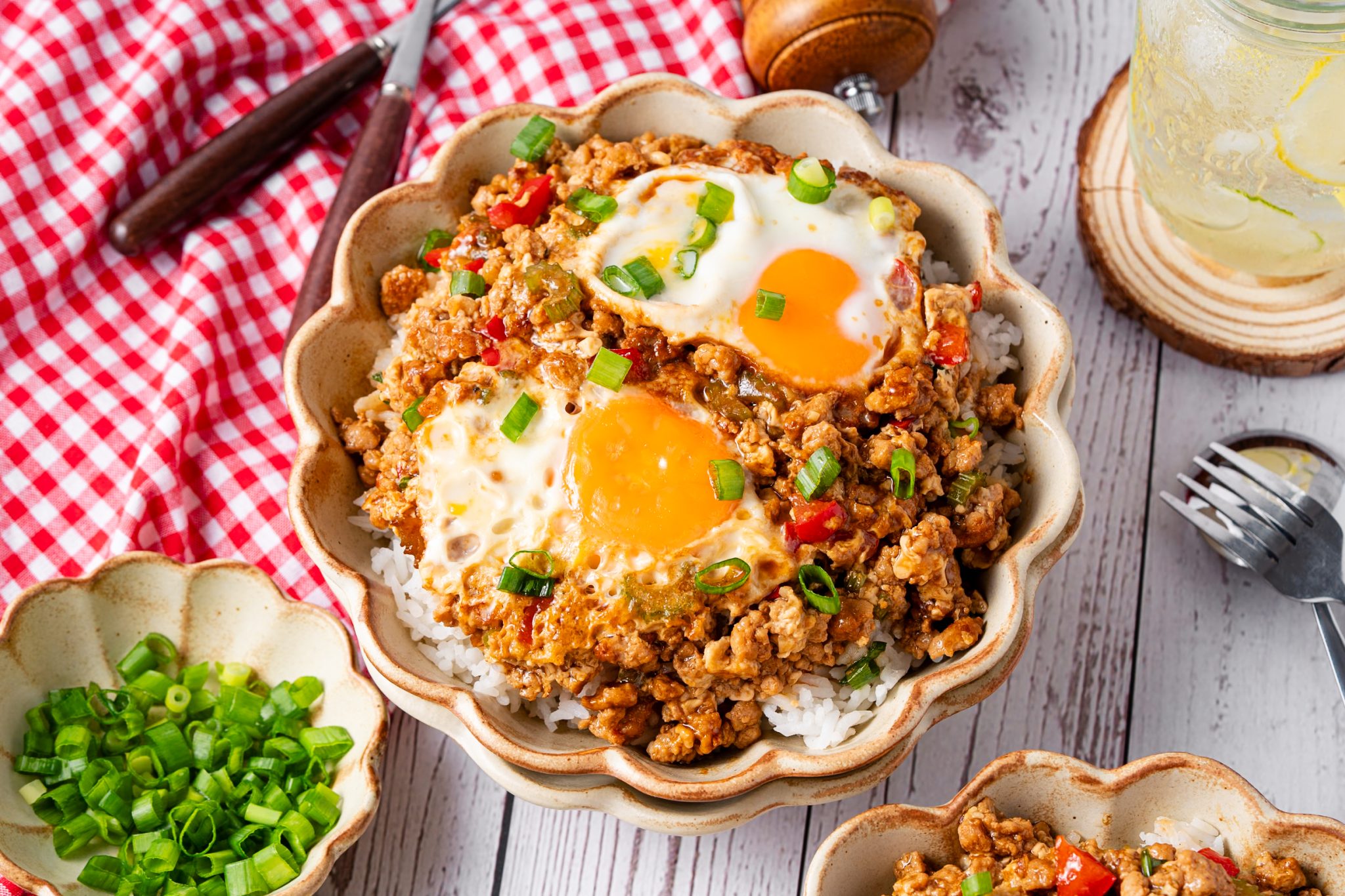 Close-up of minced meat and egg rice bowl with runny egg yolks, green onions, and red bell peppers.