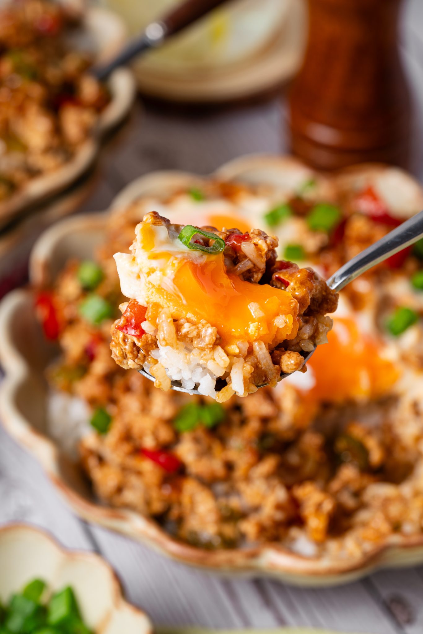 Spoonful of minced meat rice bowl with runny egg yolk, white rice, red peppers, and scallions.